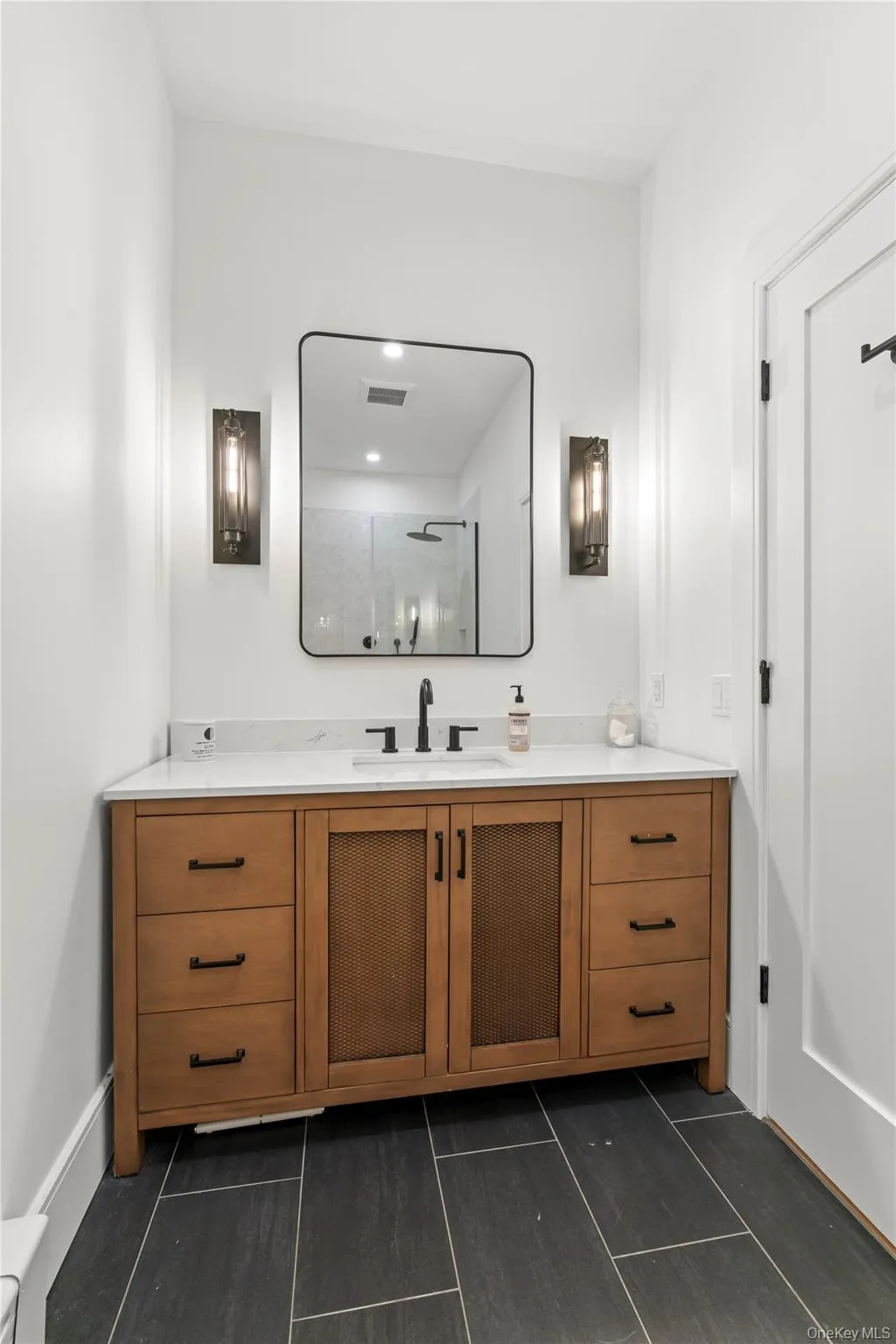 LowerBathroom featuring a wood-finish vanity with ample storage, a white countertop, and a rectangular black-framed mirror LowerBathroom featuring a wood-finish vanity with ample storage, a white countertop, and a rectangular black-framed mirror