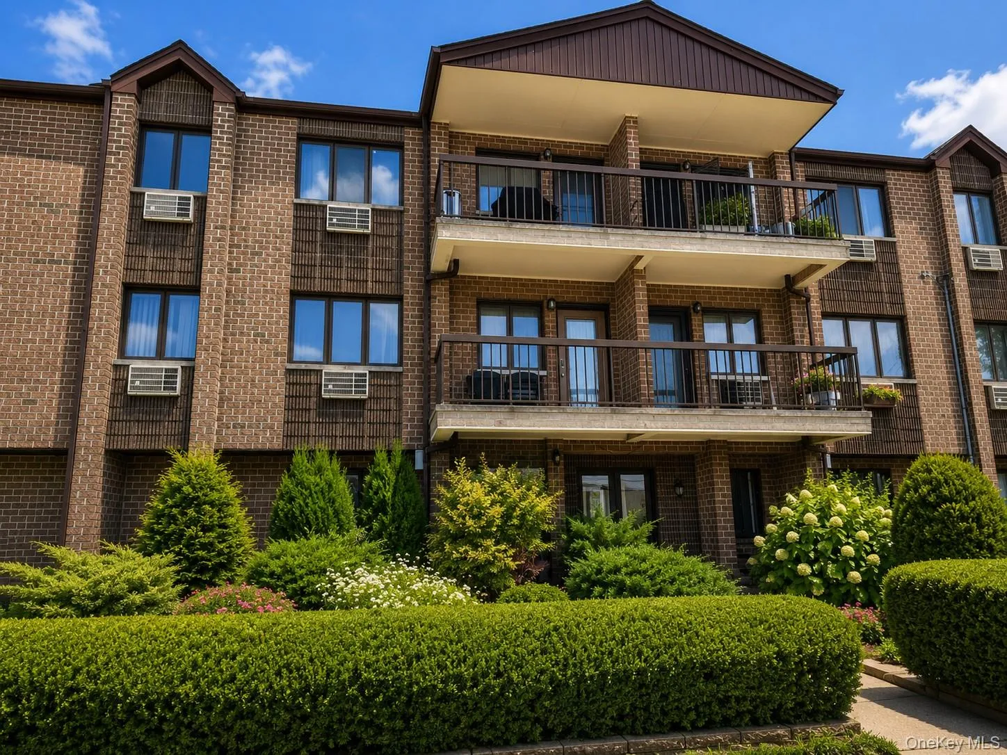 Brick facade building featuring multiple balconies with dark iron railings and an architectural shingle roofline Brick facade building featuring multiple balconies with dark iron railings and an architectural shingle roofline