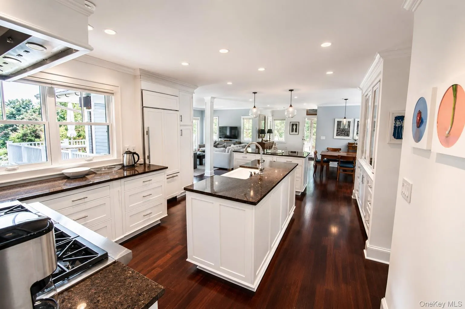 Gourmet kitchen featuring rich wood-finish flooring, white cabinetry, dark stone countertops, and a central island with sink Gourmet kitchen featuring rich wood-finish flooring, white cabinetry, dark stone countertops, and a central island with sink