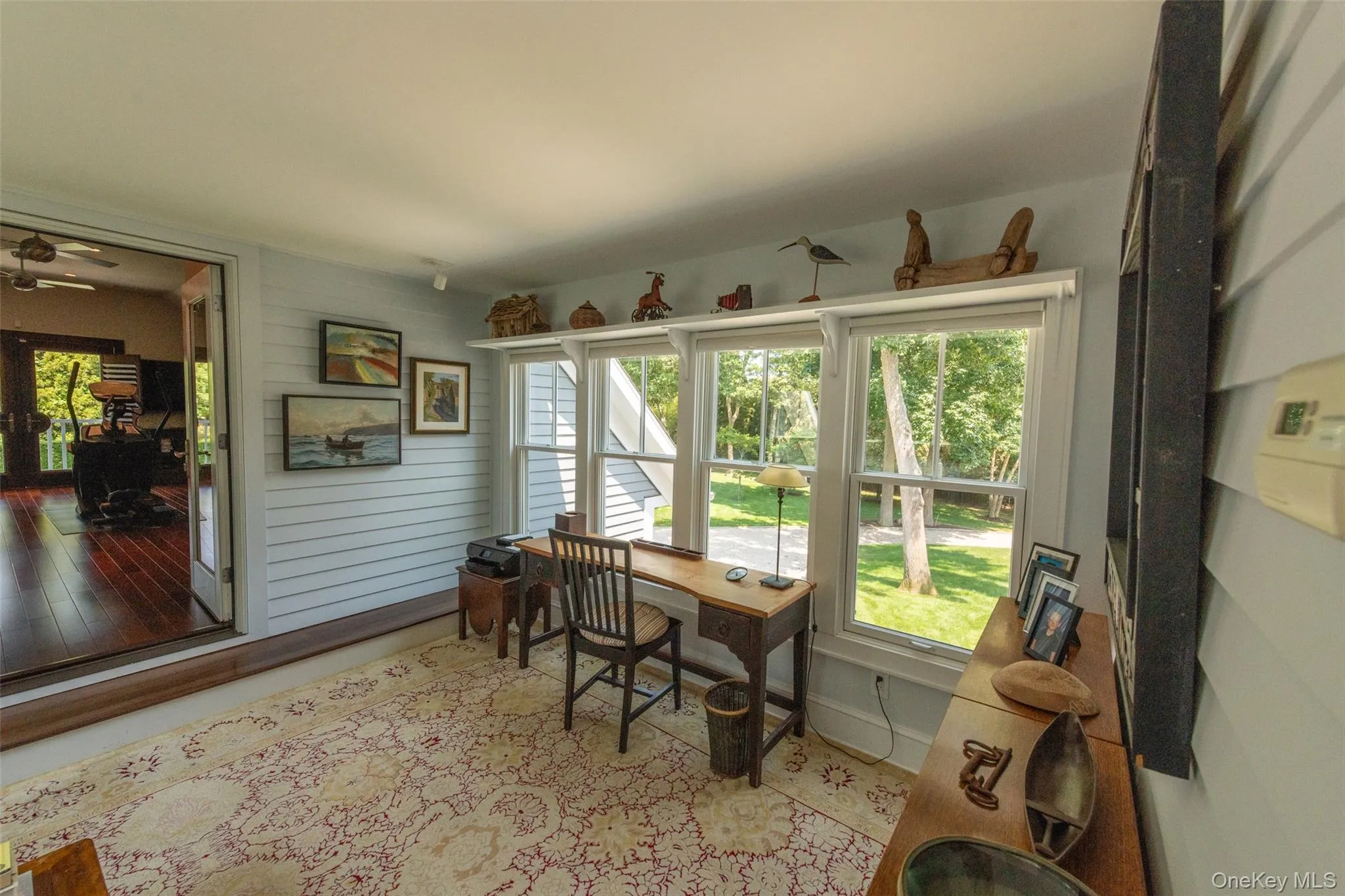 Sunroom featuring multiple windows, horizontal plank walls, a ceiling fan, and double doors opening to an interior space with wood-finish flooring Sunroom featuring multiple windows, horizontal plank walls, a ceiling fan, and double doors opening to an interior space with wood-finish flooring