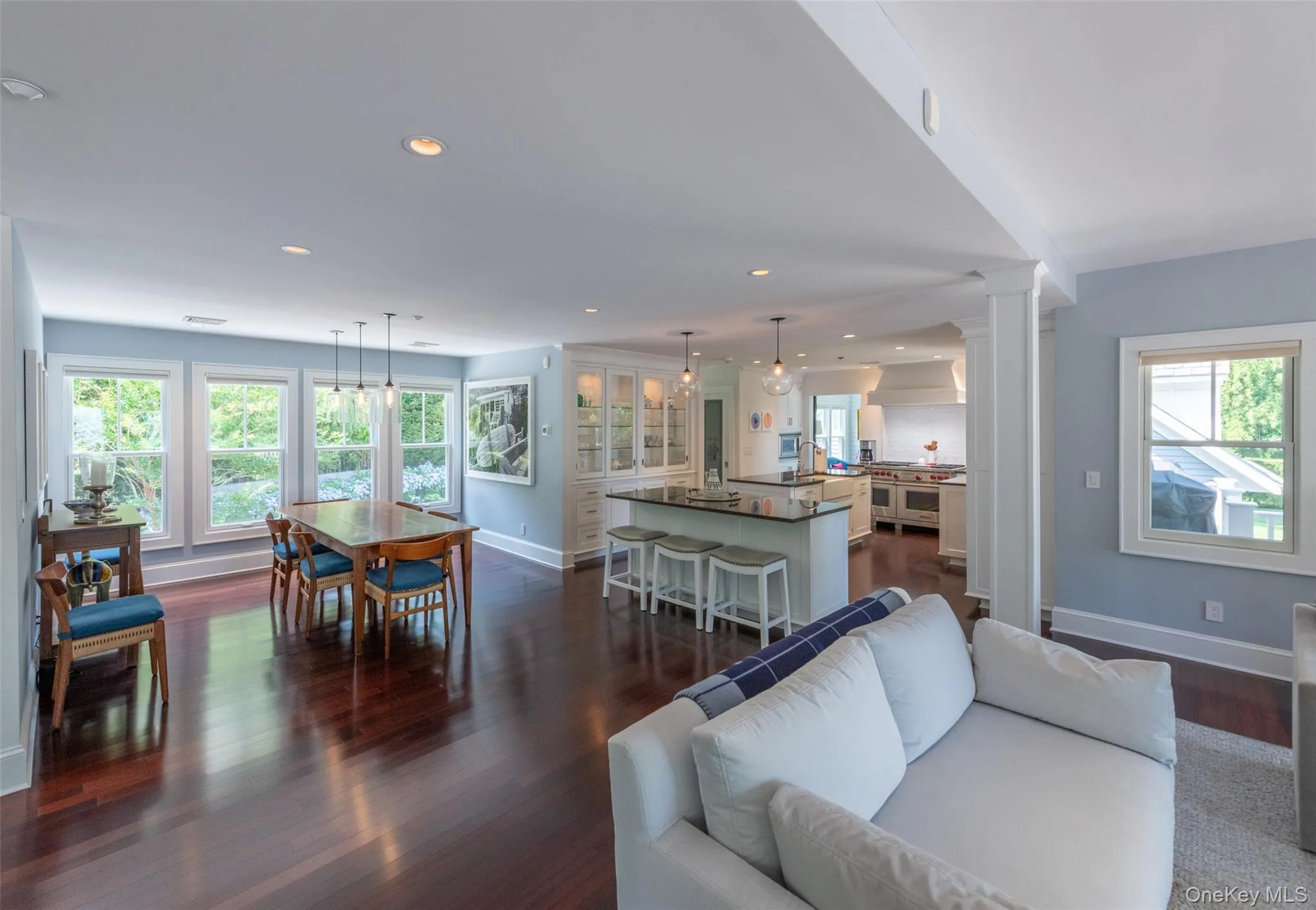 Spacious open-concept living area featuring rich wood-finish flooring, recessed lighting, and ample natural light from multiple windows Spacious open-concept living area featuring rich wood-finish flooring, recessed lighting, and ample natural light from multiple windows