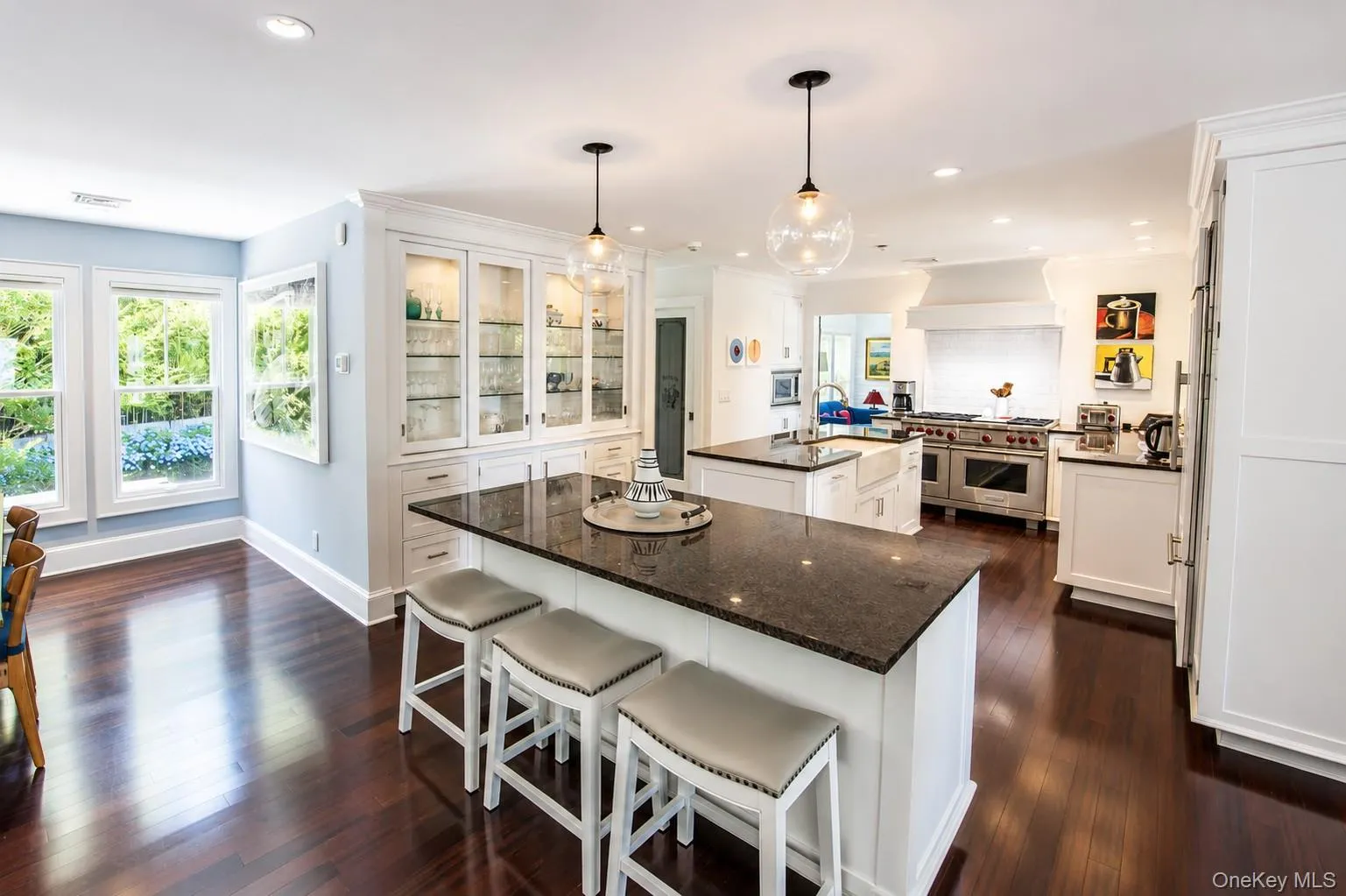 Kitchen featuring dark wood-finish flooring, white cabinetry, dark stone countertops, and a double island layout Kitchen featuring dark wood-finish flooring, white cabinetry, dark stone countertops, and a double island layout