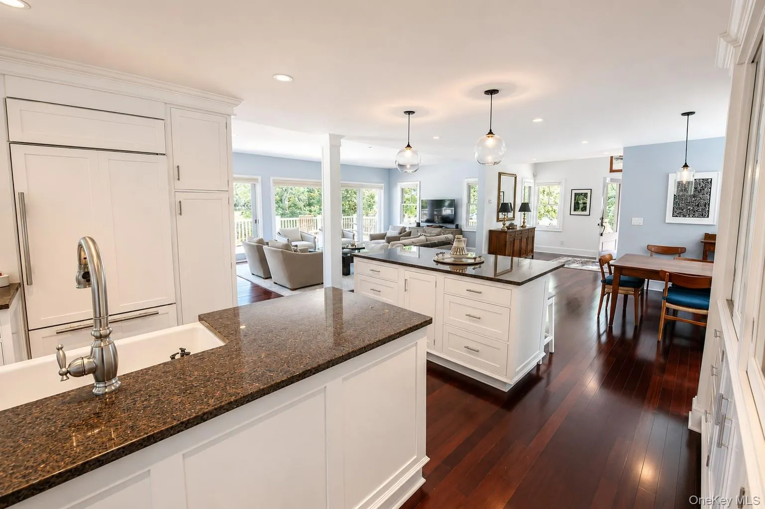Open-concept kitchen featuring white shaker cabinetry, an integrated refrigerator, a farmhouse sink, and rich wood-finish flooring Open-concept kitchen featuring white shaker cabinetry, an integrated refrigerator, a farmhouse sink, and rich wood-finish flooring