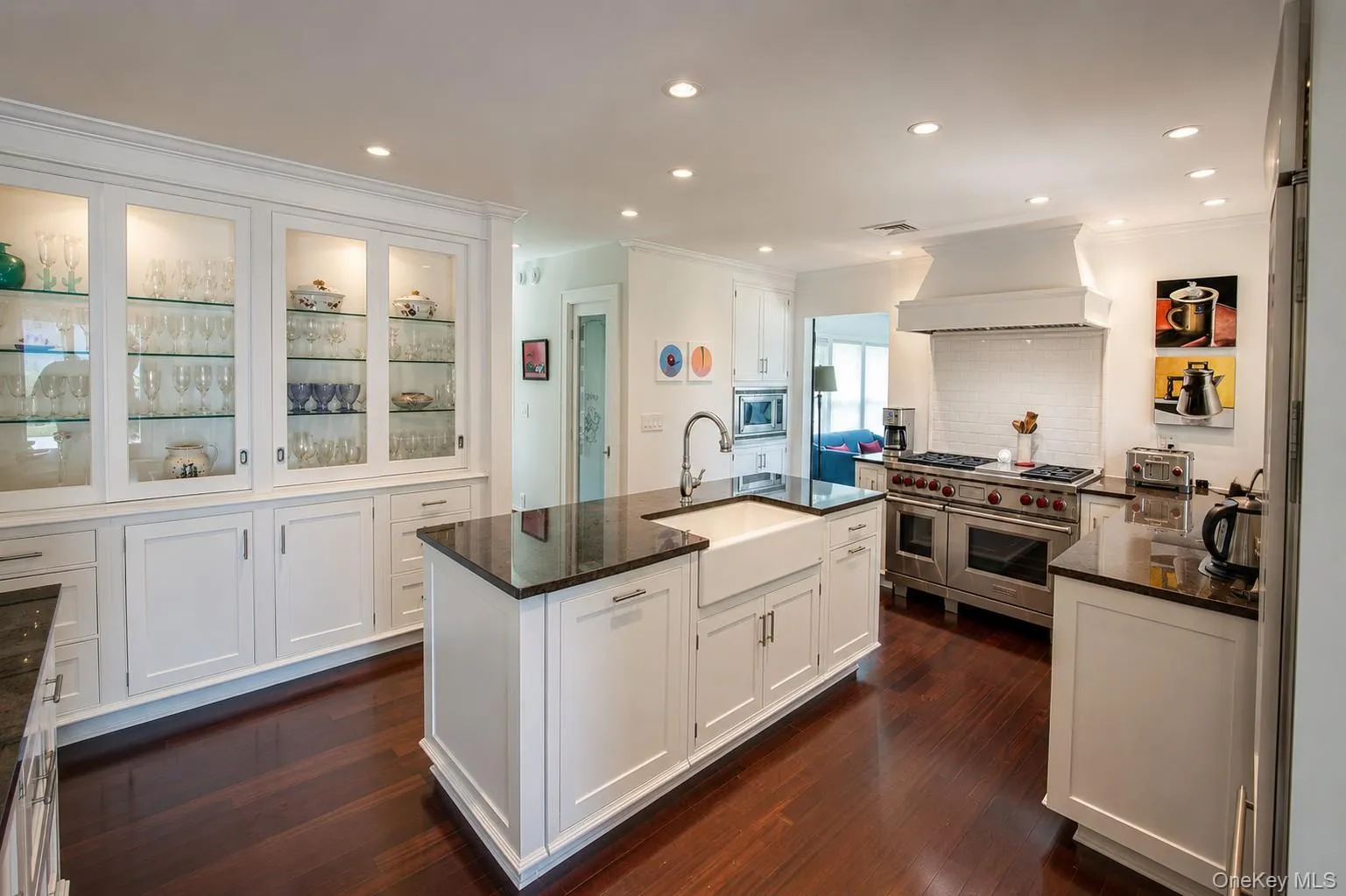 Kitchen featuring a large central island with a farmhouse sink, stainless steel appliances, dark wood-finish flooring, white cabinetry, and recessed lighting Kitchen featuring a large central island with a farmhouse sink, stainless steel appliances, dark wood-finish flooring, white cabinetry, and recessed lighting