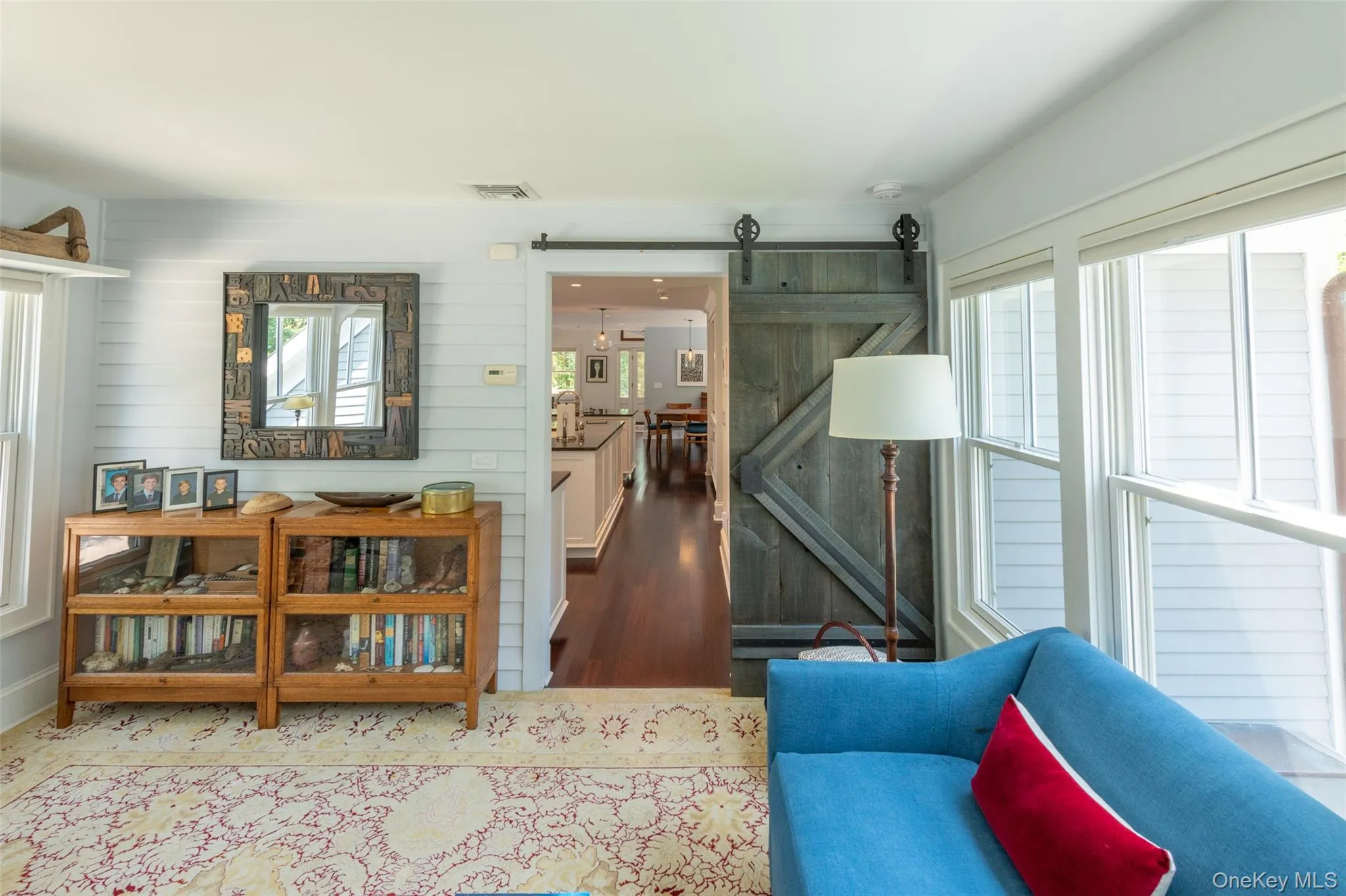 Interior space featuring a wood-finish barn door with exposed hardware, white shiplap wall paneling, and large windows Interior space featuring a wood-finish barn door with exposed hardware, white shiplap wall paneling, and large windows