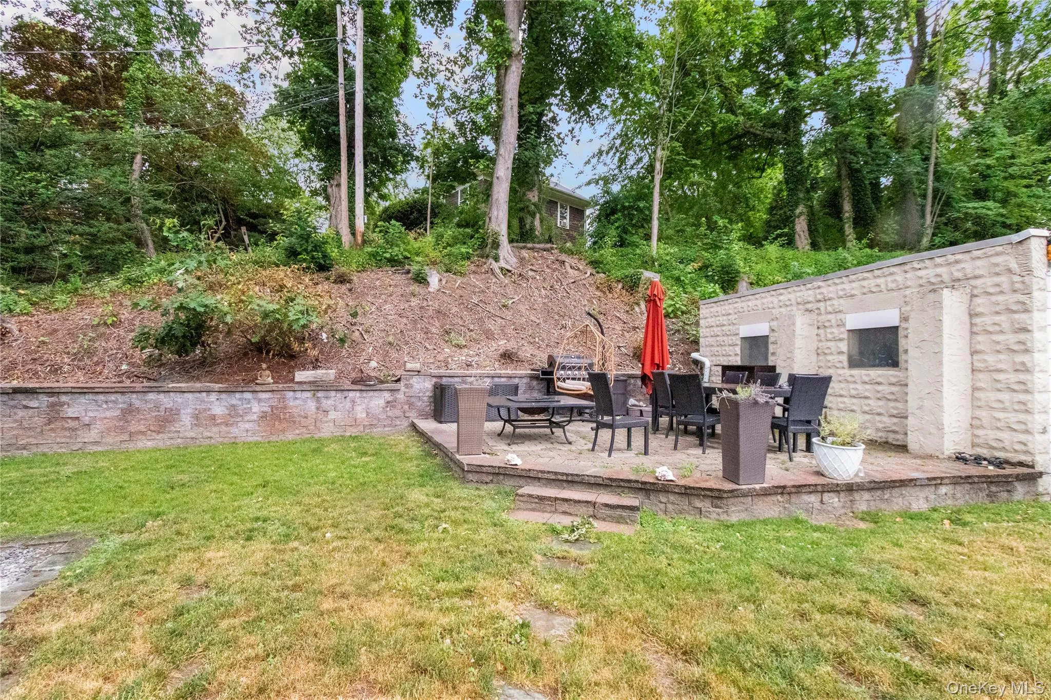 Tiered stone patio featuring a dining area, built-in stone retaining wall, and a textured stucco exterior wall Tiered stone patio featuring a dining area, built-in stone retaining wall, and a textured stucco exterior wall