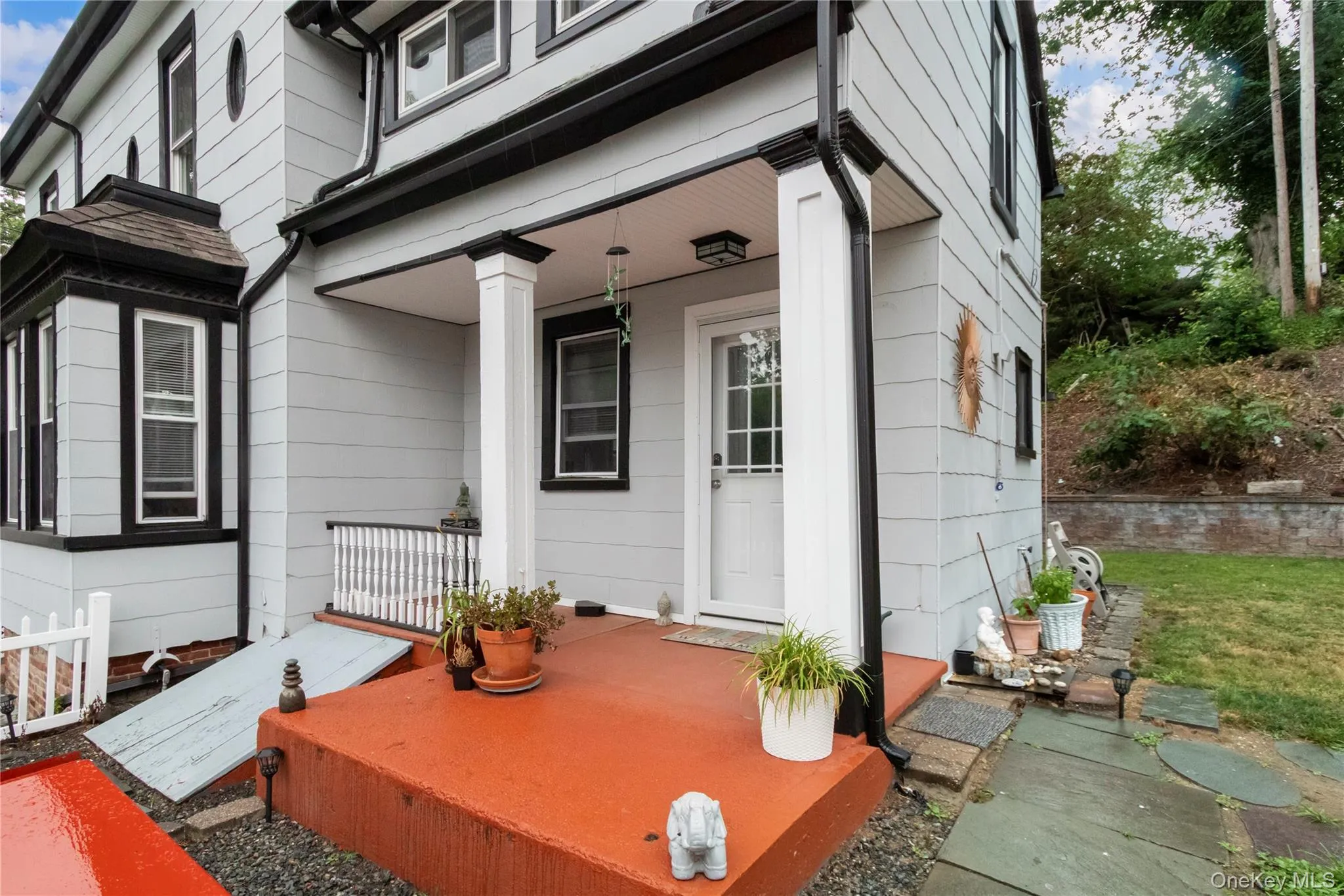 Exterior facade with light gray siding and black trim, featuring a covered front porch with white columns, an orange-painted concrete porch, and a bay window Exterior facade with light gray siding and black trim, featuring a covered front porch with white columns, an orange-painted concrete porch, and a bay window
