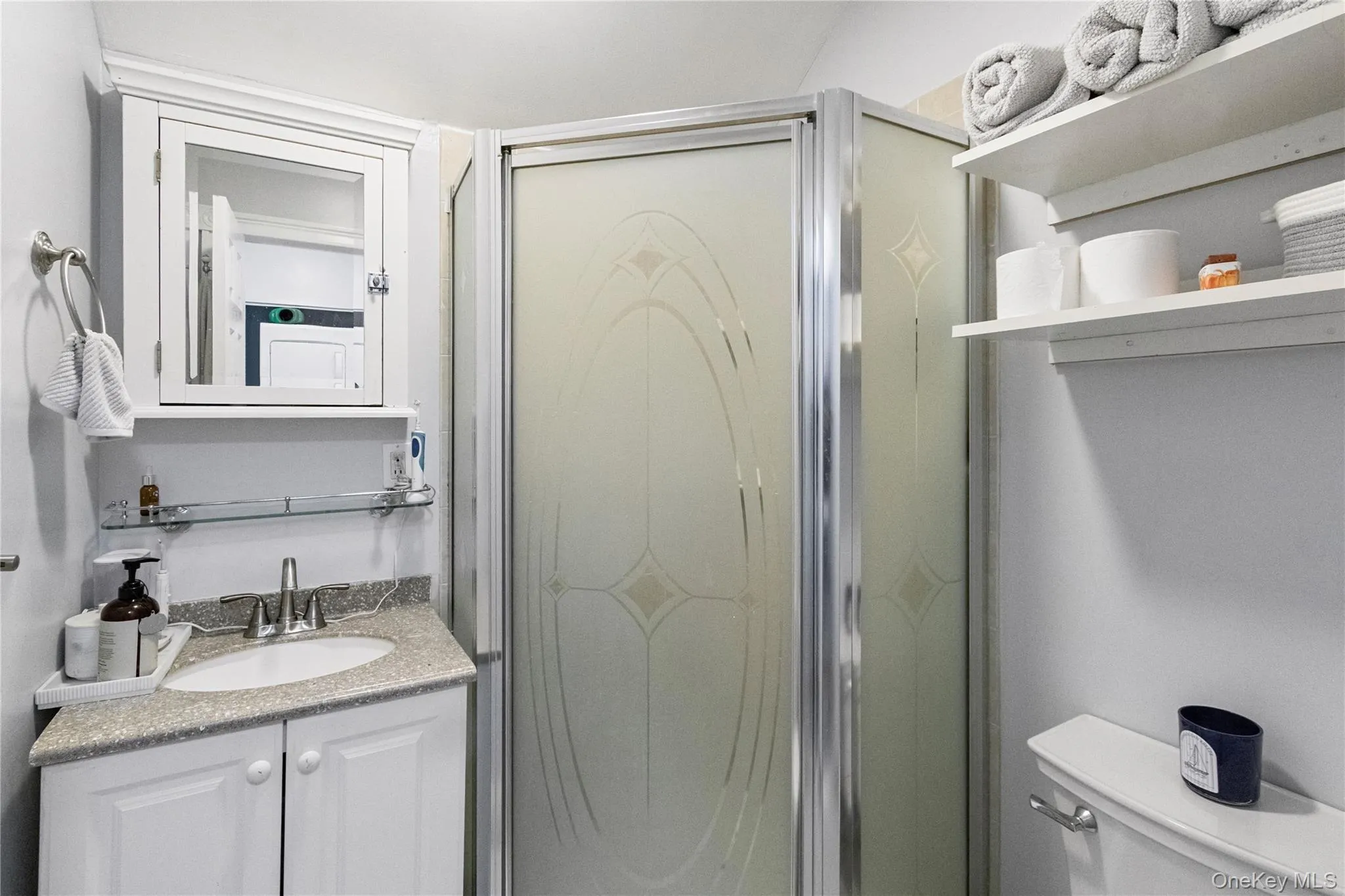 Compact bathroom featuring a corner vanity with a light-colored countertop, an oval undermount sink, and a chrome faucet Compact bathroom featuring a corner vanity with a light-colored countertop, an oval undermount sink, and a chrome faucet