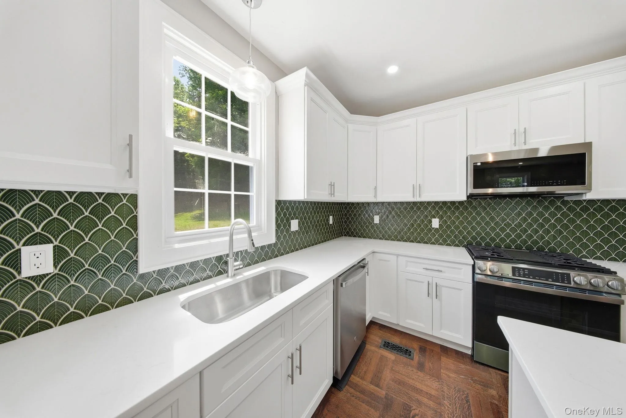 Kitchen featuring white shaker cabinetry, stainless steel appliances, a deep basin sink, dark green geometric tile backsplash, and white countertops Kitchen featuring white shaker cabinetry, stainless steel appliances, a deep basin sink, dark green geometric tile backsplash, and white countertops