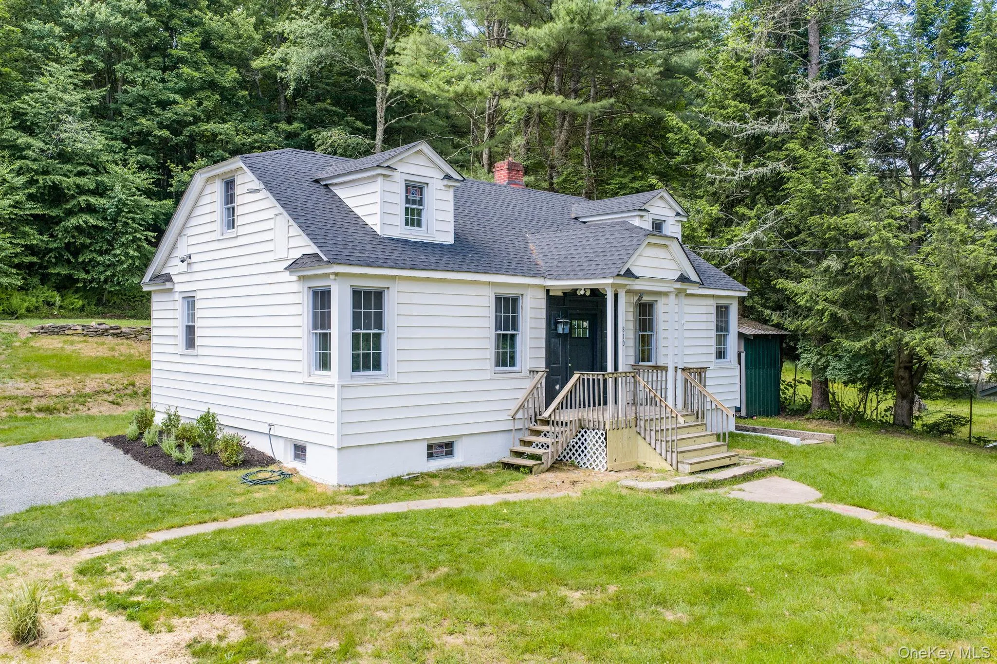 White clapboard siding exterior with a dark shingle roof, dormer windows, a covered front entry, and a gravel driveway White clapboard siding exterior with a dark shingle roof, dormer windows, a covered front entry, and a gravel driveway