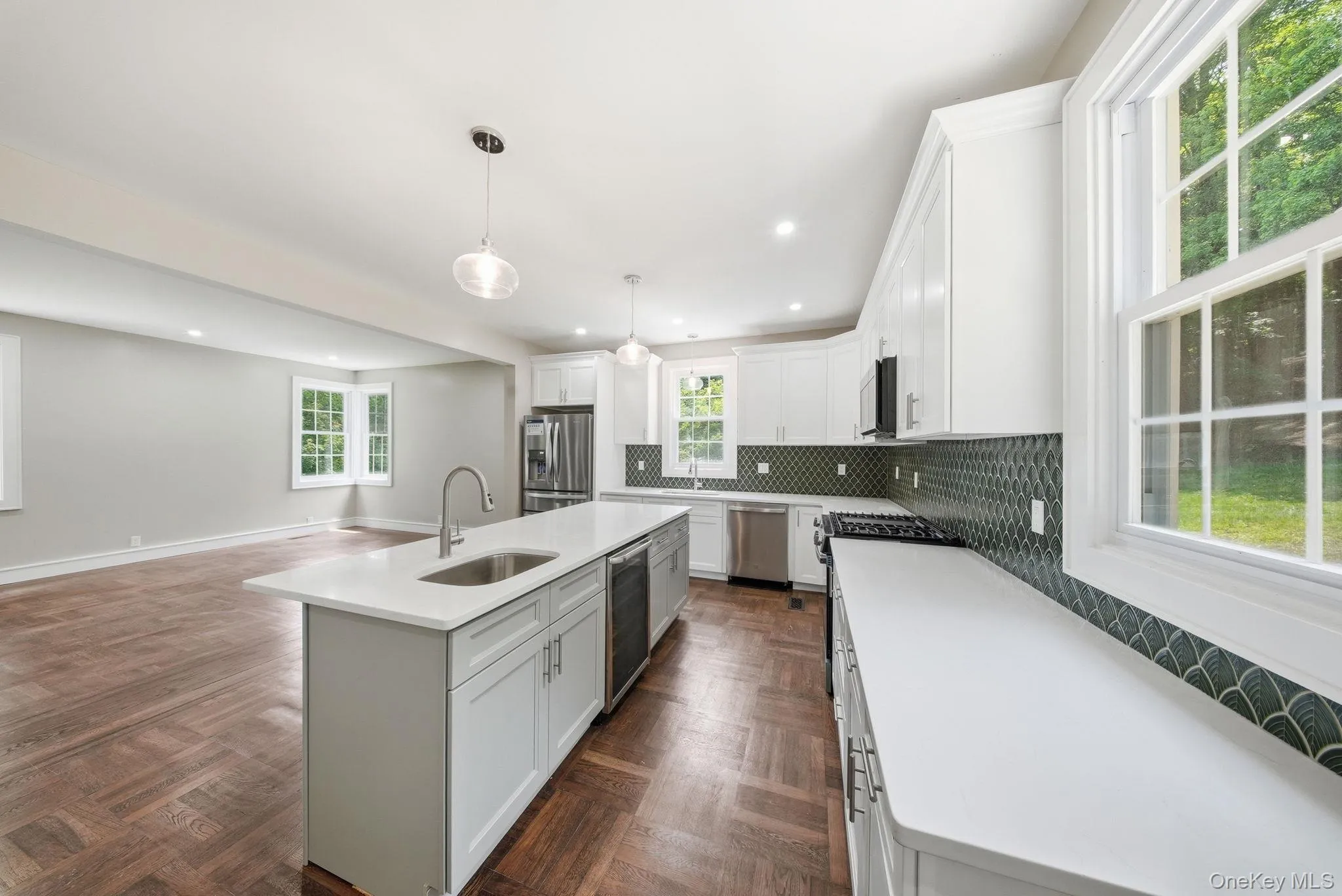Kitchen featuring white cabinetry, stainless steel appliances, a center island with sink, and dark green patterned backsplash Kitchen featuring white cabinetry, stainless steel appliances, a center island with sink, and dark green patterned backsplash