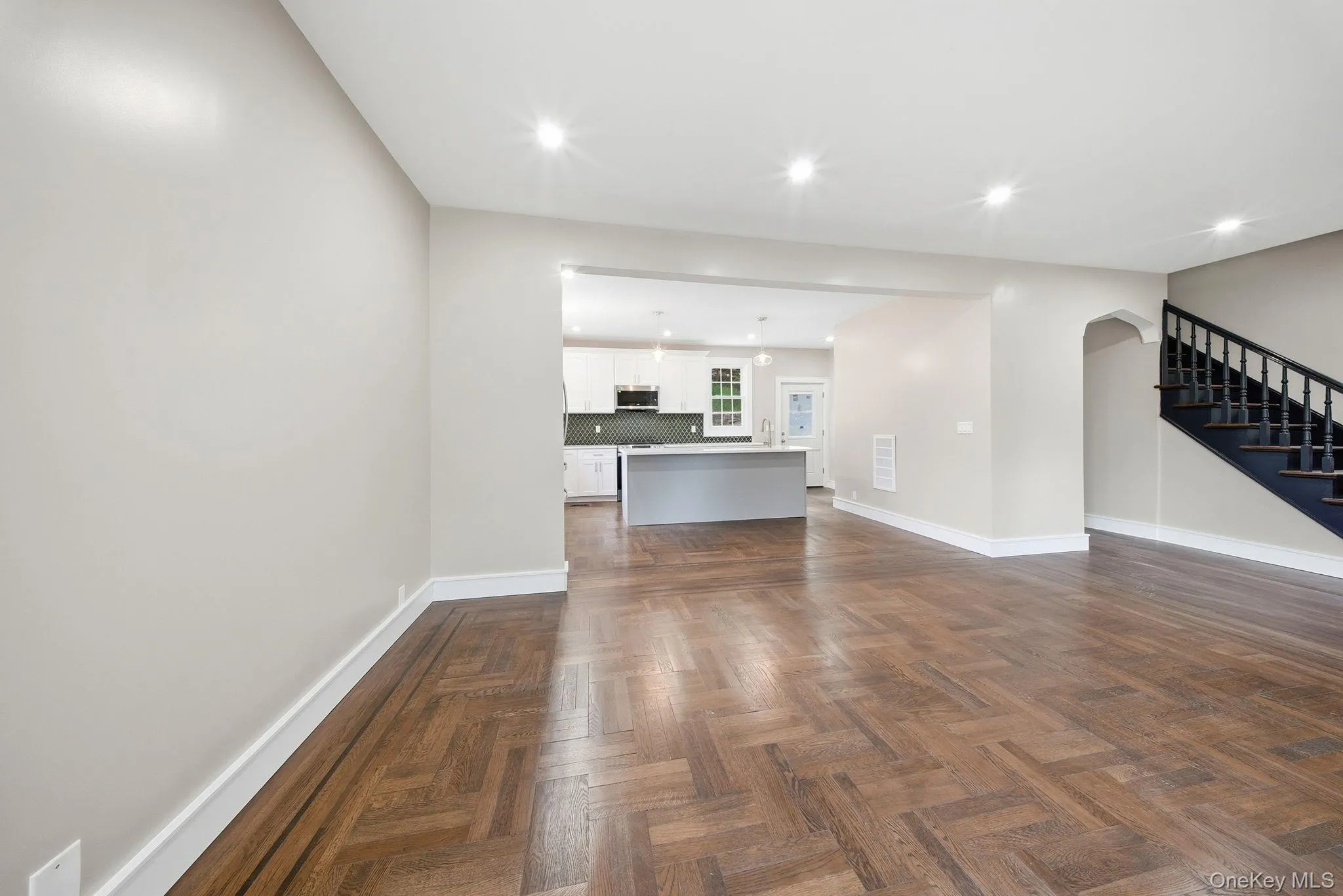 Expansive living space featuring herringbone wood-finish flooring, recessed lighting, and a defined entryway to the kitchen Expansive living space featuring herringbone wood-finish flooring, recessed lighting, and a defined entryway to the kitchen