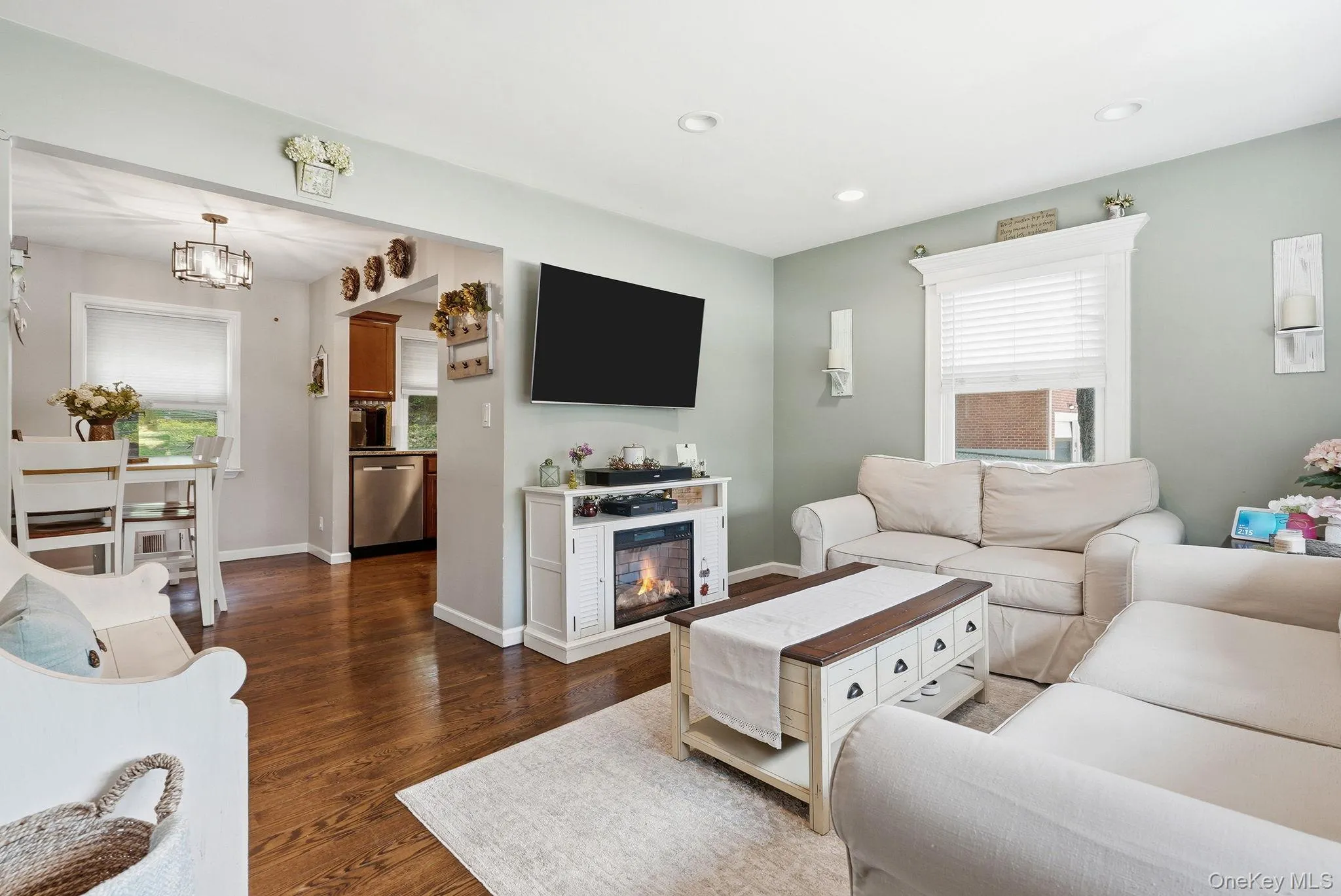 Spacious living area featuring wood-finish flooring, recessed lighting, and a decorative fireplace console Spacious living area featuring wood-finish flooring, recessed lighting, and a decorative fireplace console