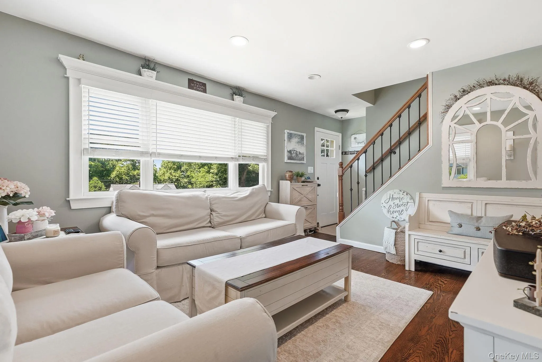 Warm and inviting living space featuring wood-finish flooring, recessed lighting, and a prominent window with horizontal blinds Warm and inviting living space featuring wood-finish flooring, recessed lighting, and a prominent window with horizontal blinds