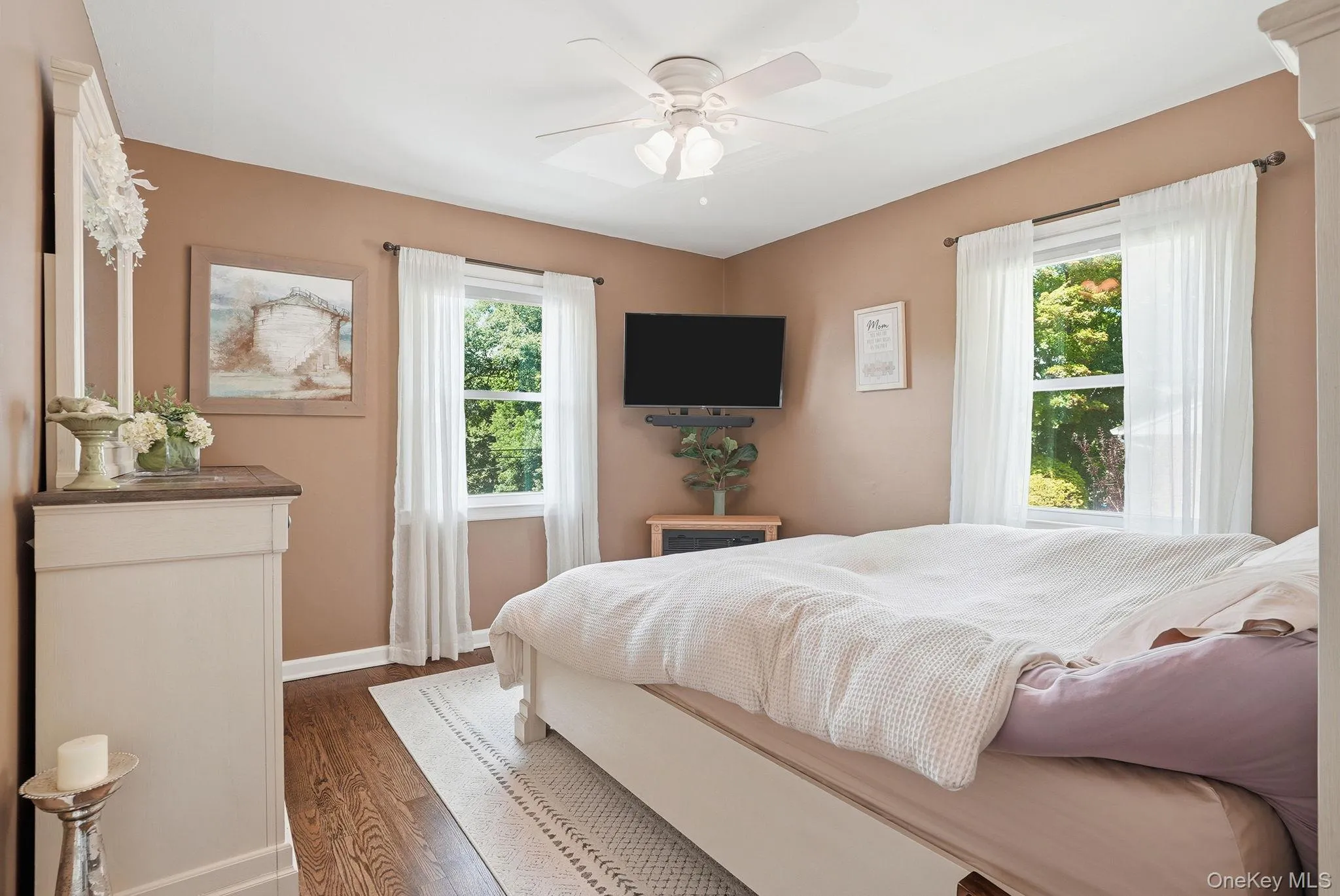 Bedroom featuring wood-finish flooring, two windows with white curtains, and a ceiling fan Bedroom featuring wood-finish flooring, two windows with white curtains, and a ceiling fan