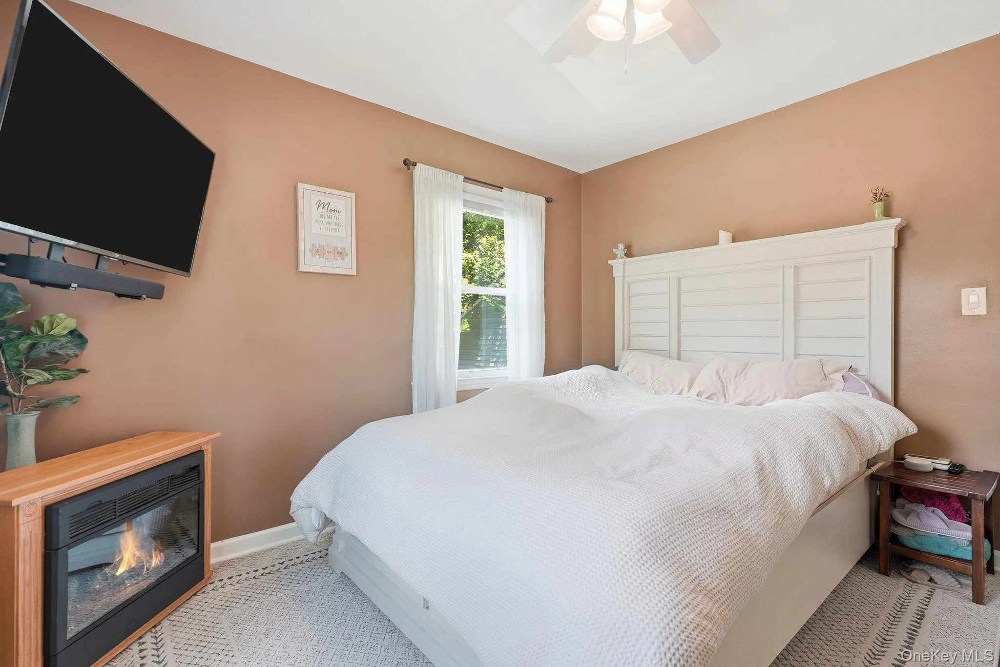 Bedroom with a ceiling fan, wall-mounted television, and an electric fireplace feature Bedroom with a ceiling fan, wall-mounted television, and an electric fireplace feature