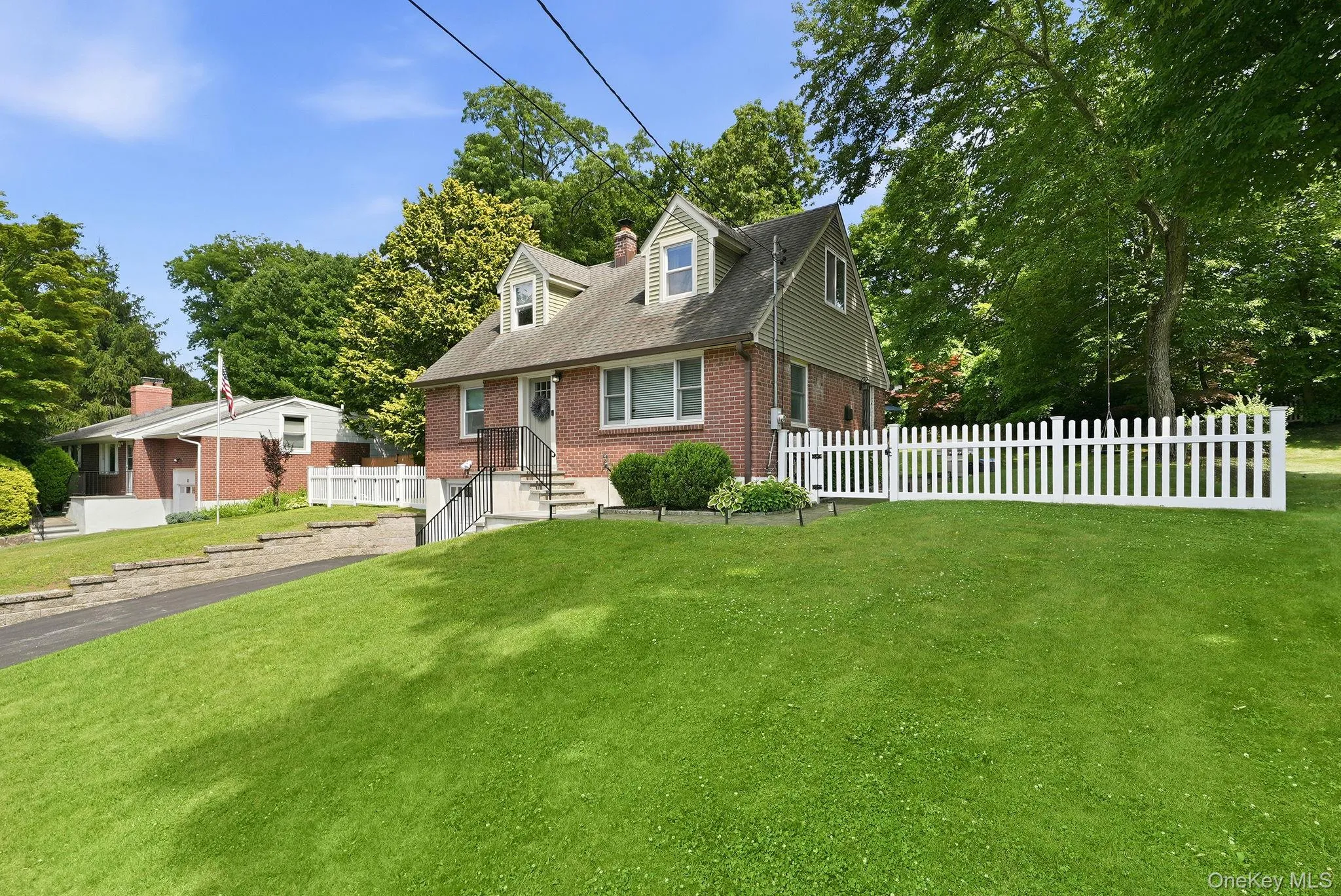 Traditional brick and siding exterior with a pitched roof, front dormer windows, and a white picket fence Traditional brick and siding exterior with a pitched roof, front dormer windows, and a white picket fence