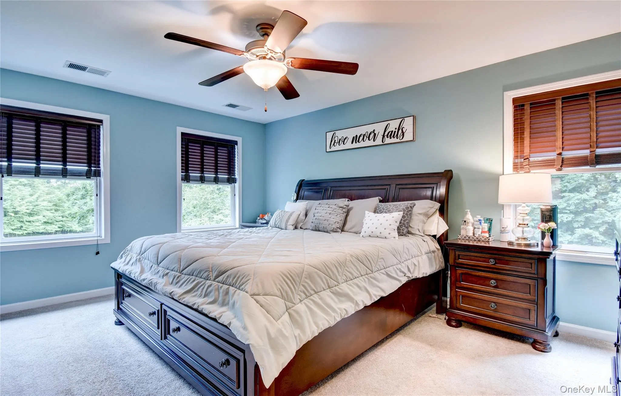 Carpeted primary bedroom featuring a ceiling fan with integrated lighting, two windows with wood slat blinds Carpeted primary bedroom featuring a ceiling fan with integrated lighting, two windows with wood slat blinds