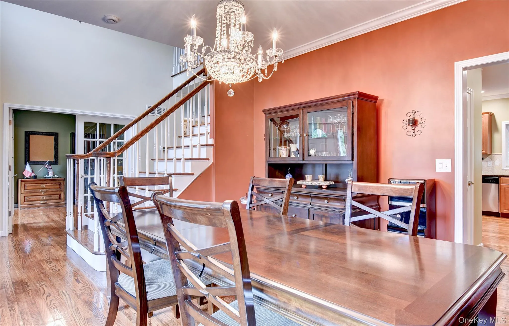 Hardwood flooring throughout the dining area, featuring a tiered crystal chandelier, crown molding, and a staircase with white risers and wood handrails Hardwood flooring throughout the dining area, featuring a tiered crystal chandelier, crown molding, and a staircase with white risers and wood handrails