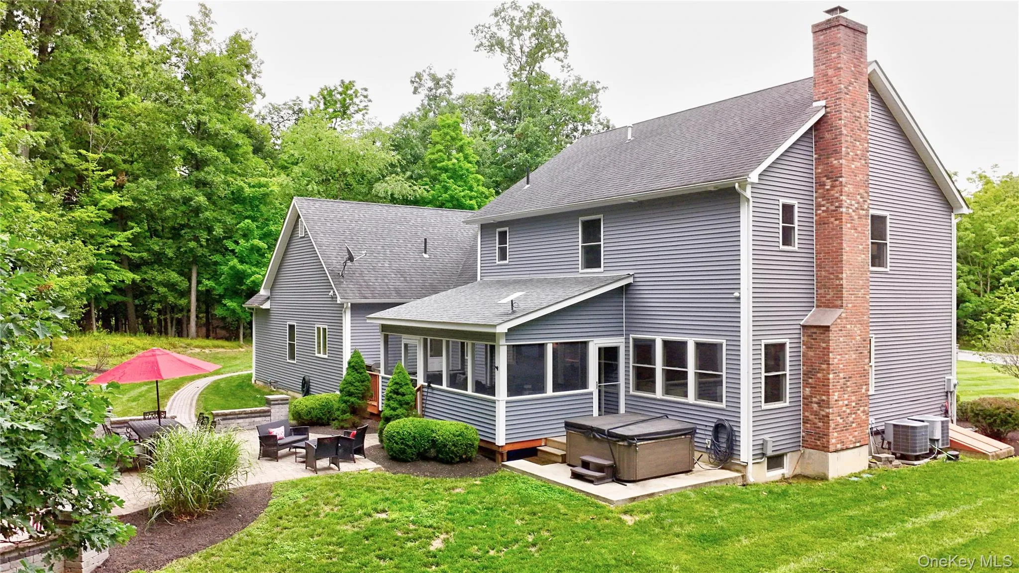 Charming Colonial-style residence featuring a gray vinyl exterior with brick chimney, complemented by a covered rear porch with black trim and railings Charming Colonial-style residence featuring a gray vinyl exterior with brick chimney, complemented by a covered rear porch with black trim and railings