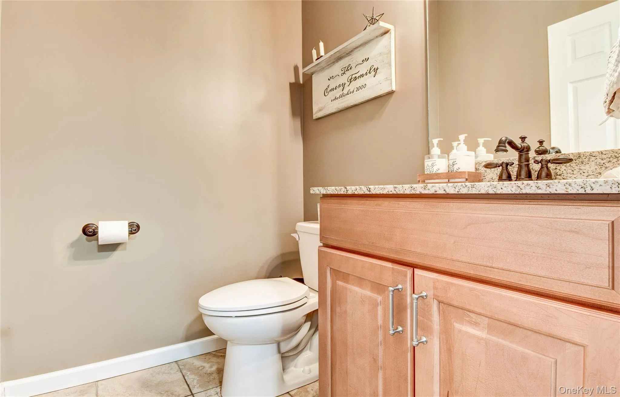 Bathroom featuring a light wood-finish vanity with paneling and brushed nickel hardware, a granite countertop, and a built-in sink with a dark-toned faucet Bathroom featuring a light wood-finish vanity with paneling and brushed nickel hardware, a granite countertop, and a built-in sink with a dark-toned faucet