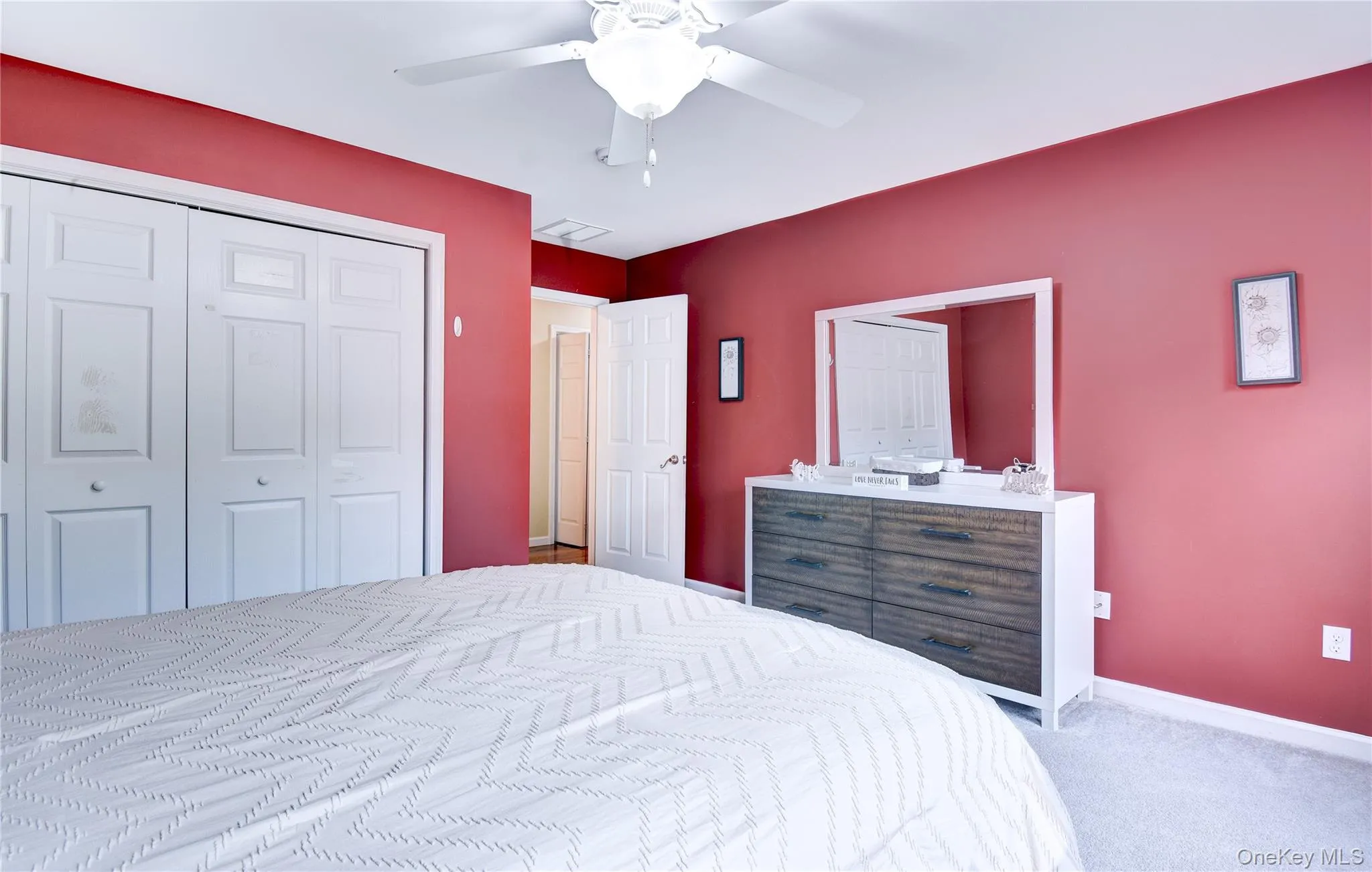 Bedroom featuring neutral-toned carpet, a ceiling fan with integrated lighting, and white bi-fold closet doors Bedroom featuring neutral-toned carpet, a ceiling fan with integrated lighting, and white bi-fold closet doors