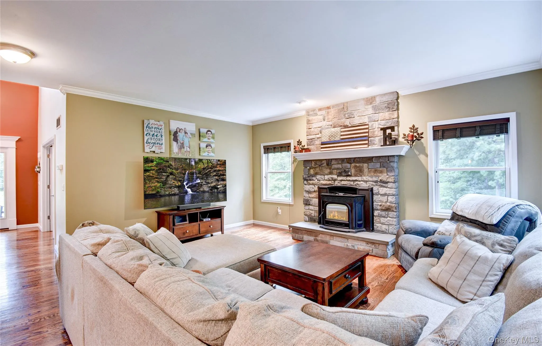 Living area featuring a stone fireplace with hearth and pellet stove, wood flooring, and crown molding Living area featuring a stone fireplace with hearth and pellet stove, wood flooring, and crown molding