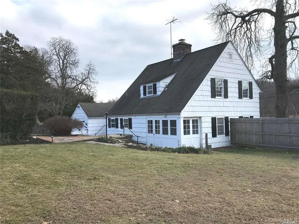 Traditional white shingle-sided residence featuring a dark shingle roof and black window shutters Traditional white shingle-sided residence featuring a dark shingle roof and black window shutters