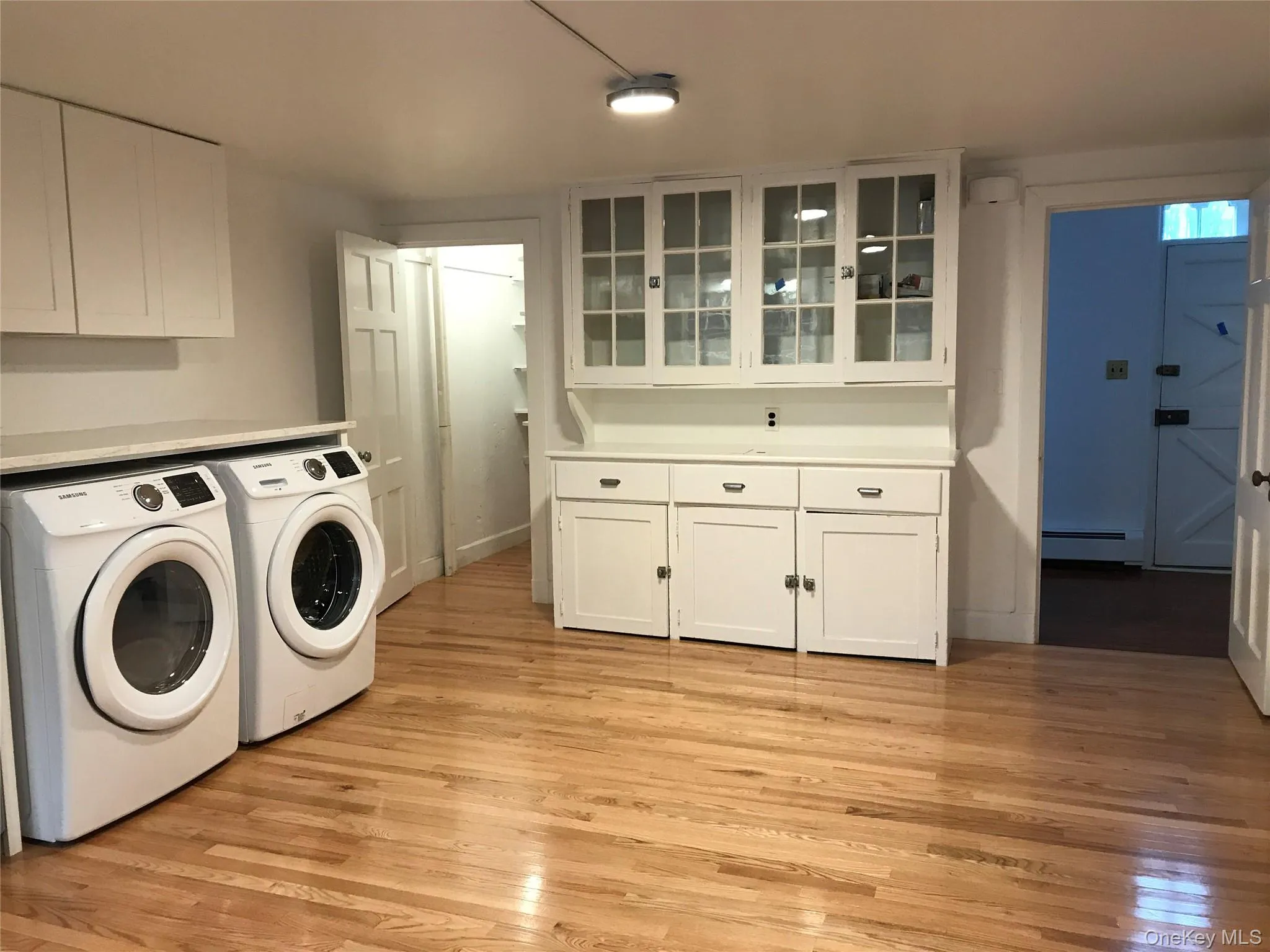 Bright utility area featuring wood-finish flooring, white built-in cabinetry, and a countertop space Bright utility area featuring wood-finish flooring, white built-in cabinetry, and a countertop space