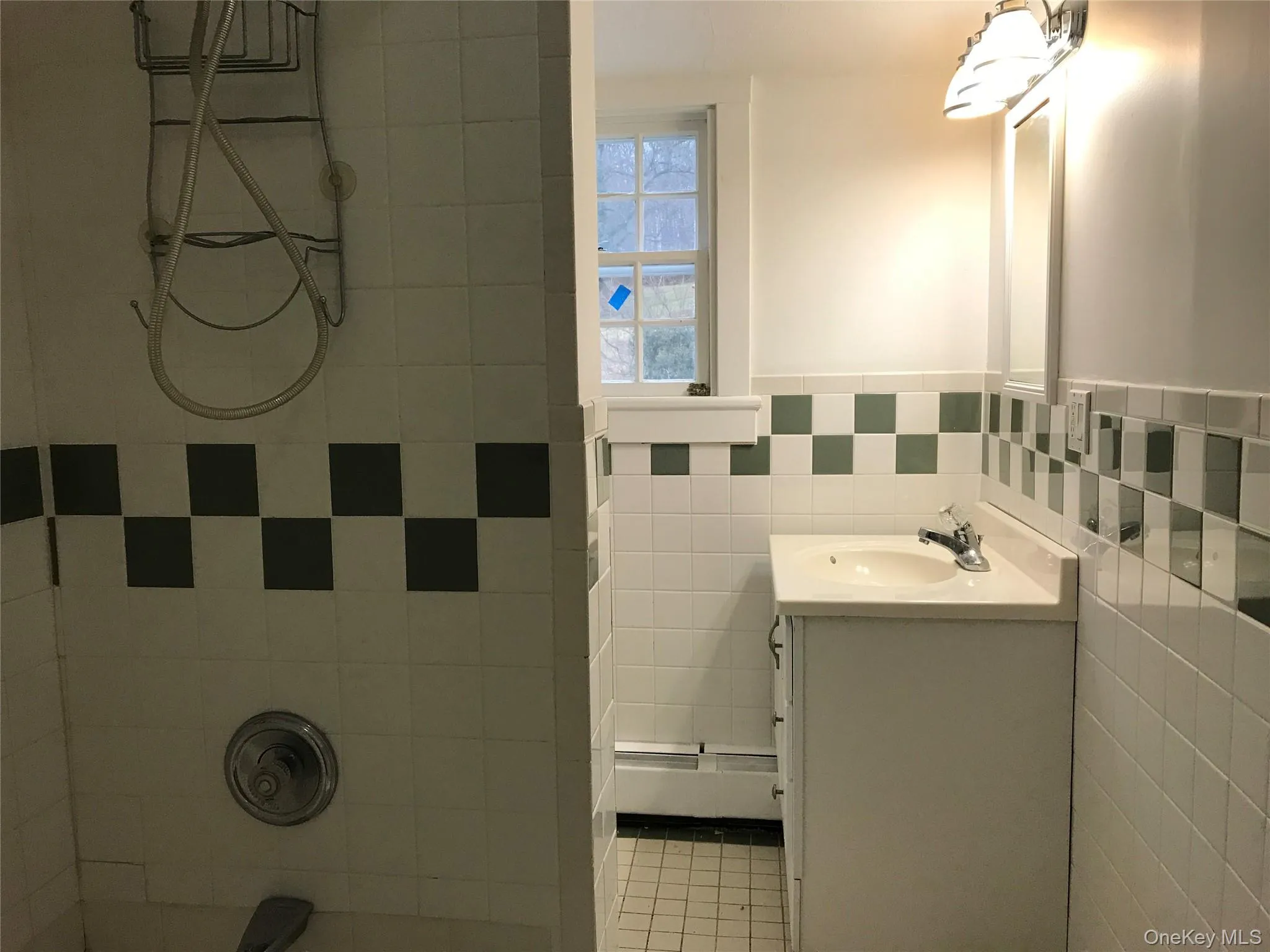 Bathroom featuring a white tile shower surround with a decorative checkerboard accent, a white vanity with an integrated sink, a wall-mounted medicine cabinet, and a window providing natural light Bathroom featuring a white tile shower surround with a decorative checkerboard accent, a white vanity with an integrated sink, a wall-mounted medicine cabinet, and a window providing natural light