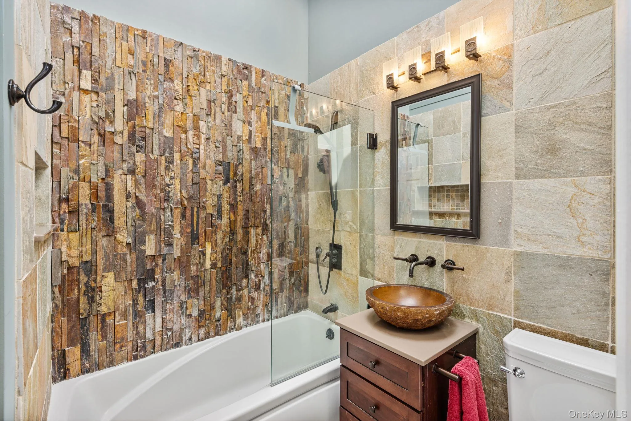 Bathroom featuring a stacked stone accent wall in the shower, a glass shower enclosure, and a vessel sink set on a wood-finish vanity Bathroom featuring a stacked stone accent wall in the shower, a glass shower enclosure, and a vessel sink set on a wood-finish vanity