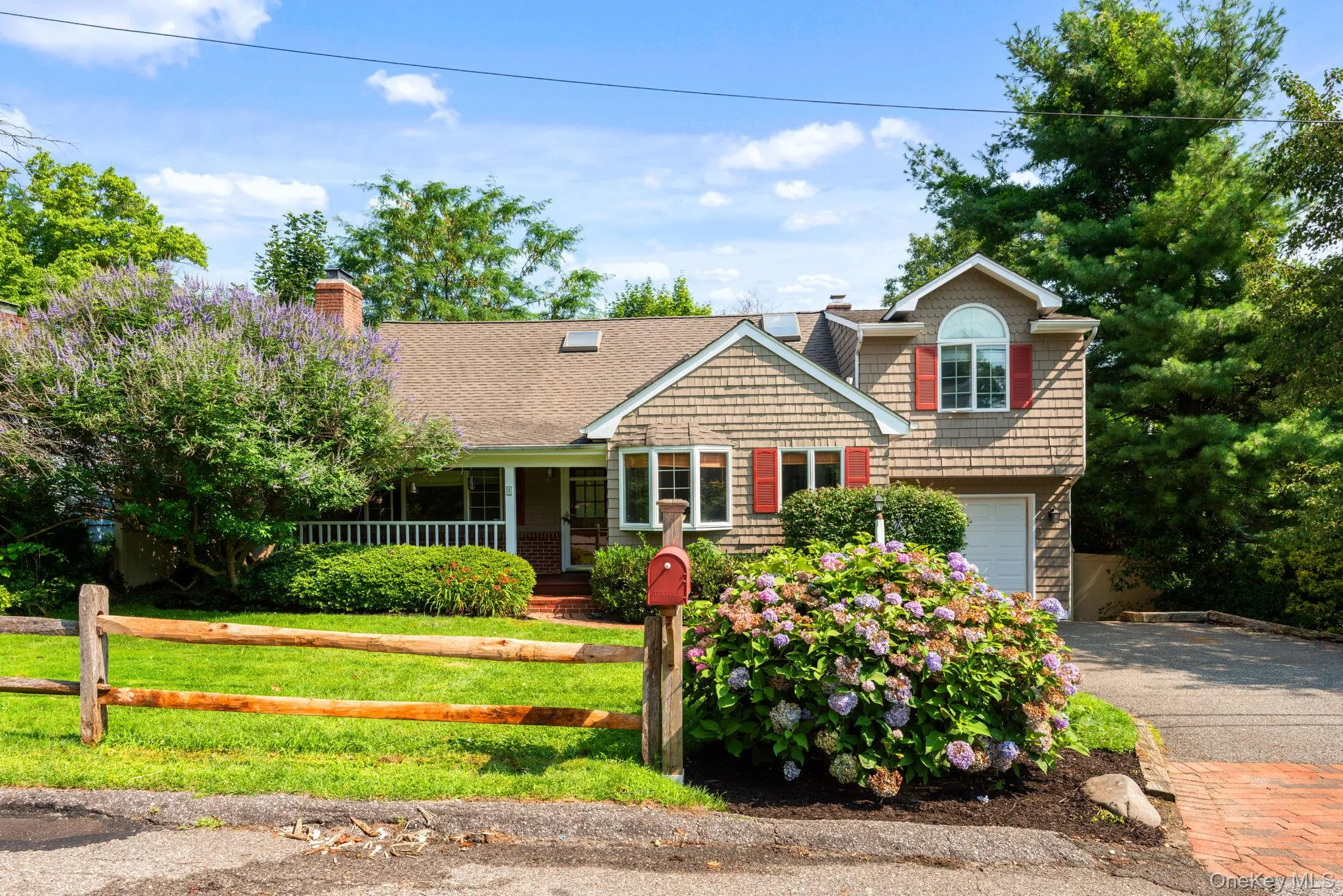 Shingle-sided residence featuring a covered porch with white railings, a bay window, and an upper-level arched window with red shutters Shingle-sided residence featuring a covered porch with white railings, a bay window, and an upper-level arched window with red shutters