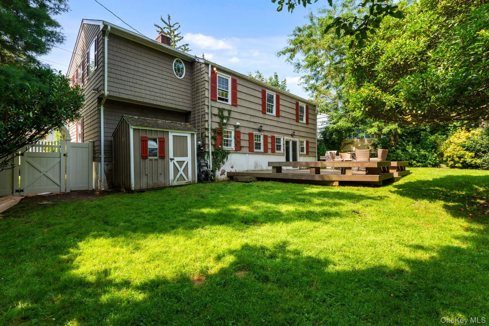 Shingle-sided back of residence featuring a spacious wood-finish deck featuring built-in seat and expansive lawn Shingle-sided back of residence featuring a spacious wood-finish deck featuring built-in seat and expansive lawn