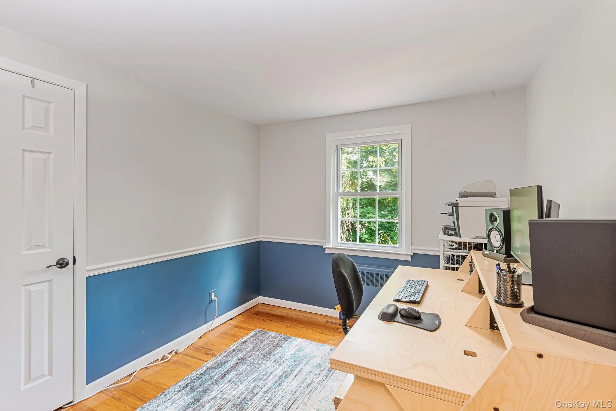 Bedroom turned office featuring wood-finish flooring, a double-hung window, and two-tone walls with chair rail molding Bedroom turned office featuring wood-finish flooring, a double-hung window, and two-tone walls with chair rail molding