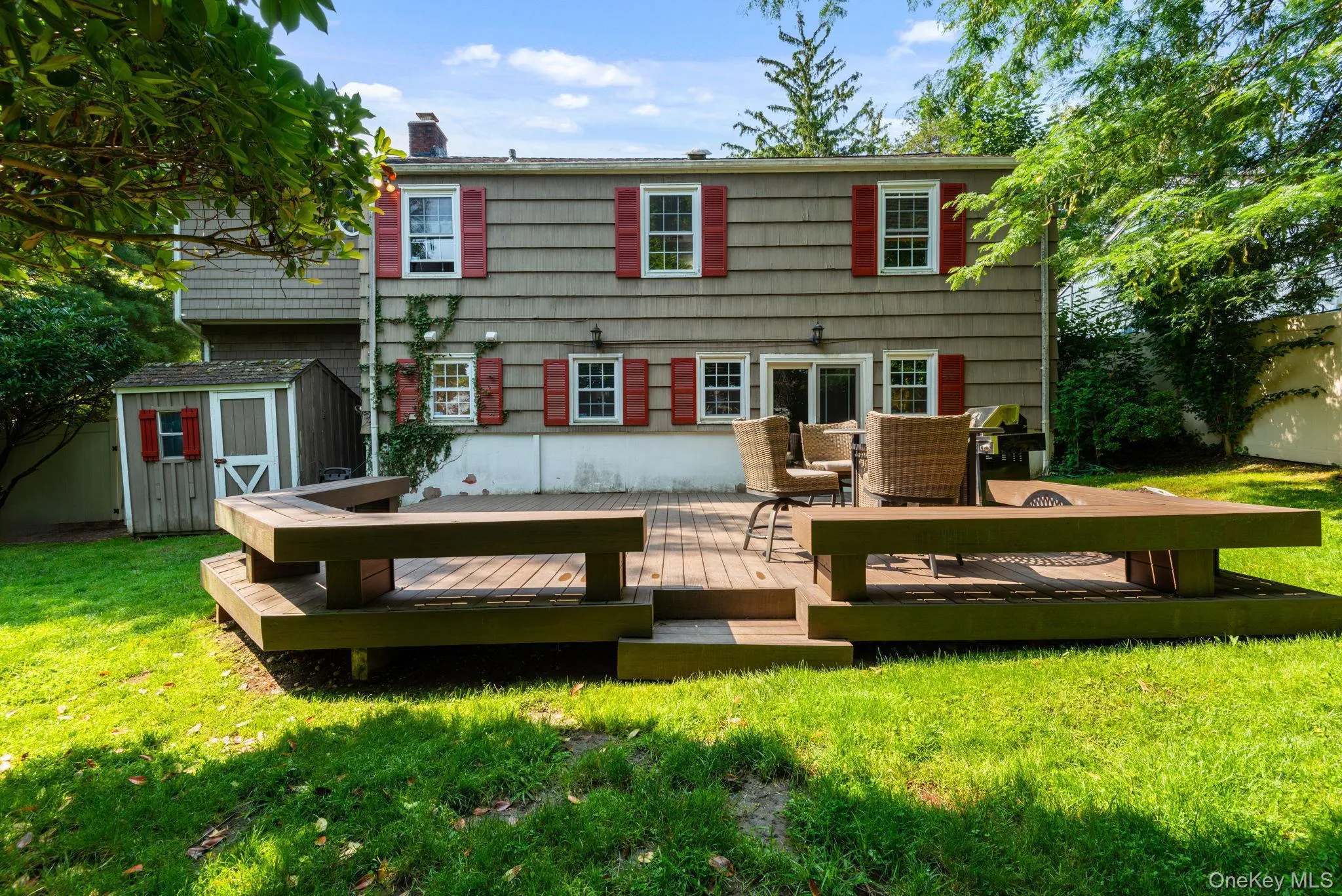 Shingle-sided back of residence featuring a spacious wood-finish deck featuring built-in seat and expansive lawn Shingle-sided back of residence featuring a spacious wood-finish deck featuring built-in seat and expansive lawn