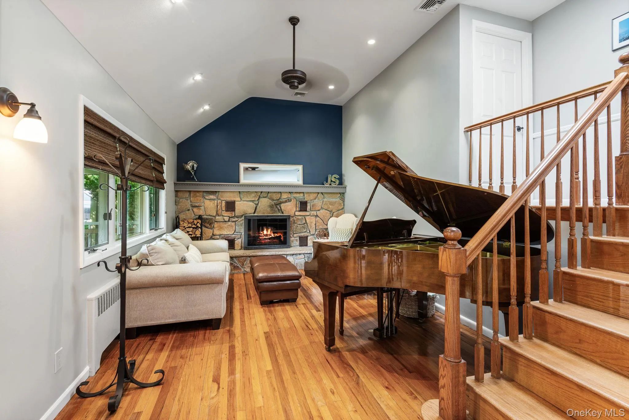Living space featuring hardwood flooring, a stone fireplace, vaulted ceiling with recessed lighting, and a staircase with a wooden banister Living space featuring hardwood flooring, a stone fireplace, vaulted ceiling with recessed lighting, and a staircase with a wooden banister