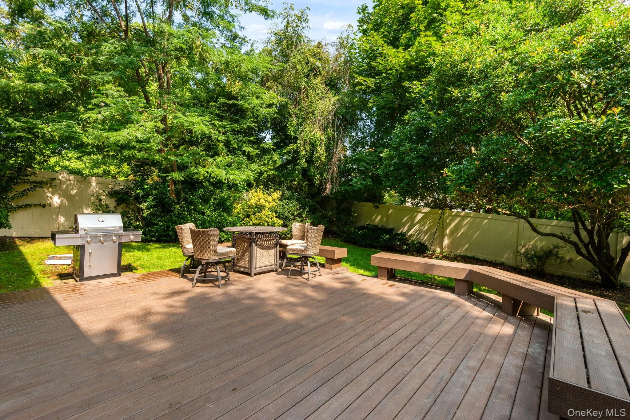 Shingle-sided back of residence featuring a spacious wood-finish deck featuring built-in seat and expansive lawn Shingle-sided back of residence featuring a spacious wood-finish deck featuring built-in seat and expansive lawn