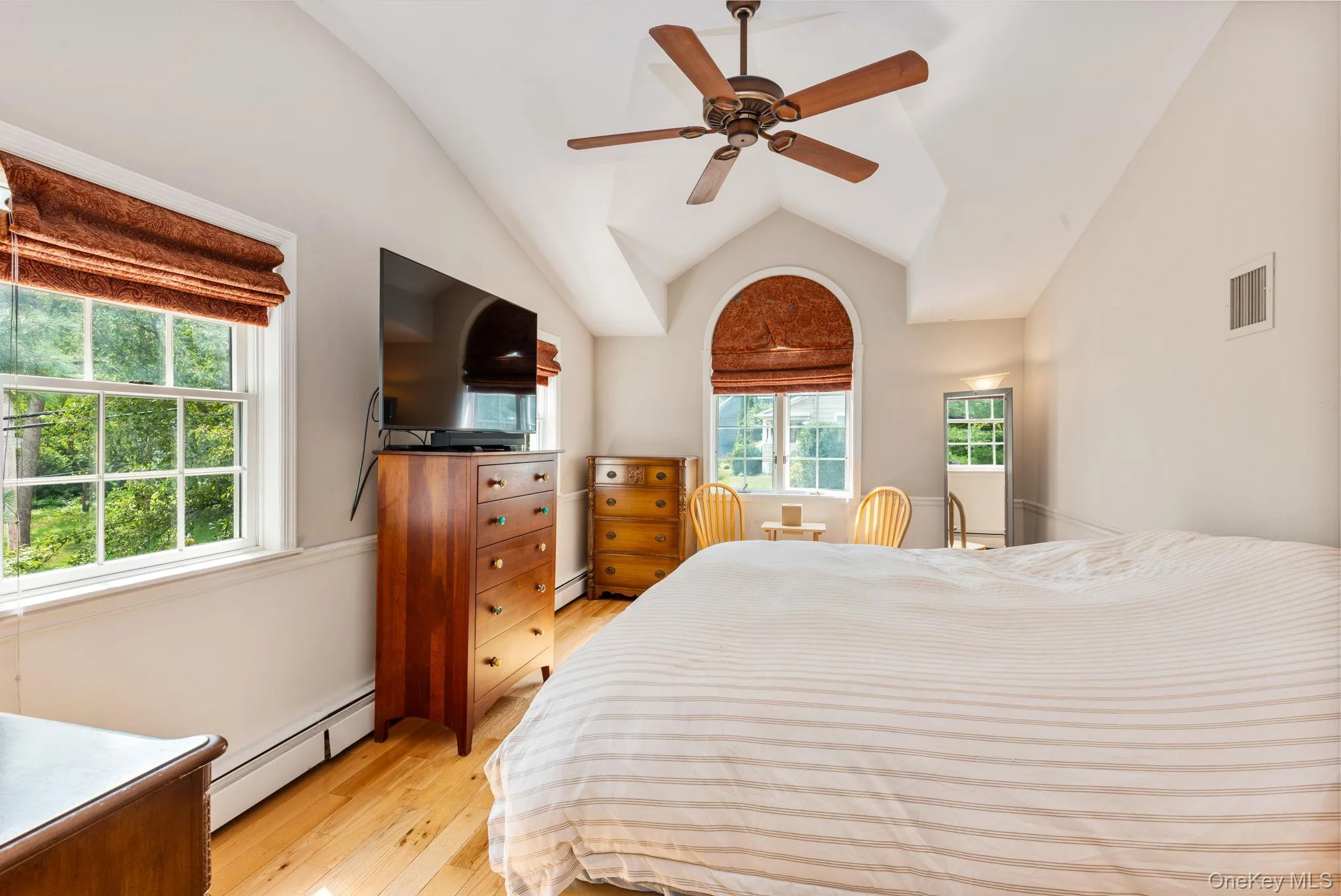 Bedroom featuring a vaulted ceiling with a ceiling fan, light wood-finish flooring, and white baseboard heating Bedroom featuring a vaulted ceiling with a ceiling fan, light wood-finish flooring, and white baseboard heating