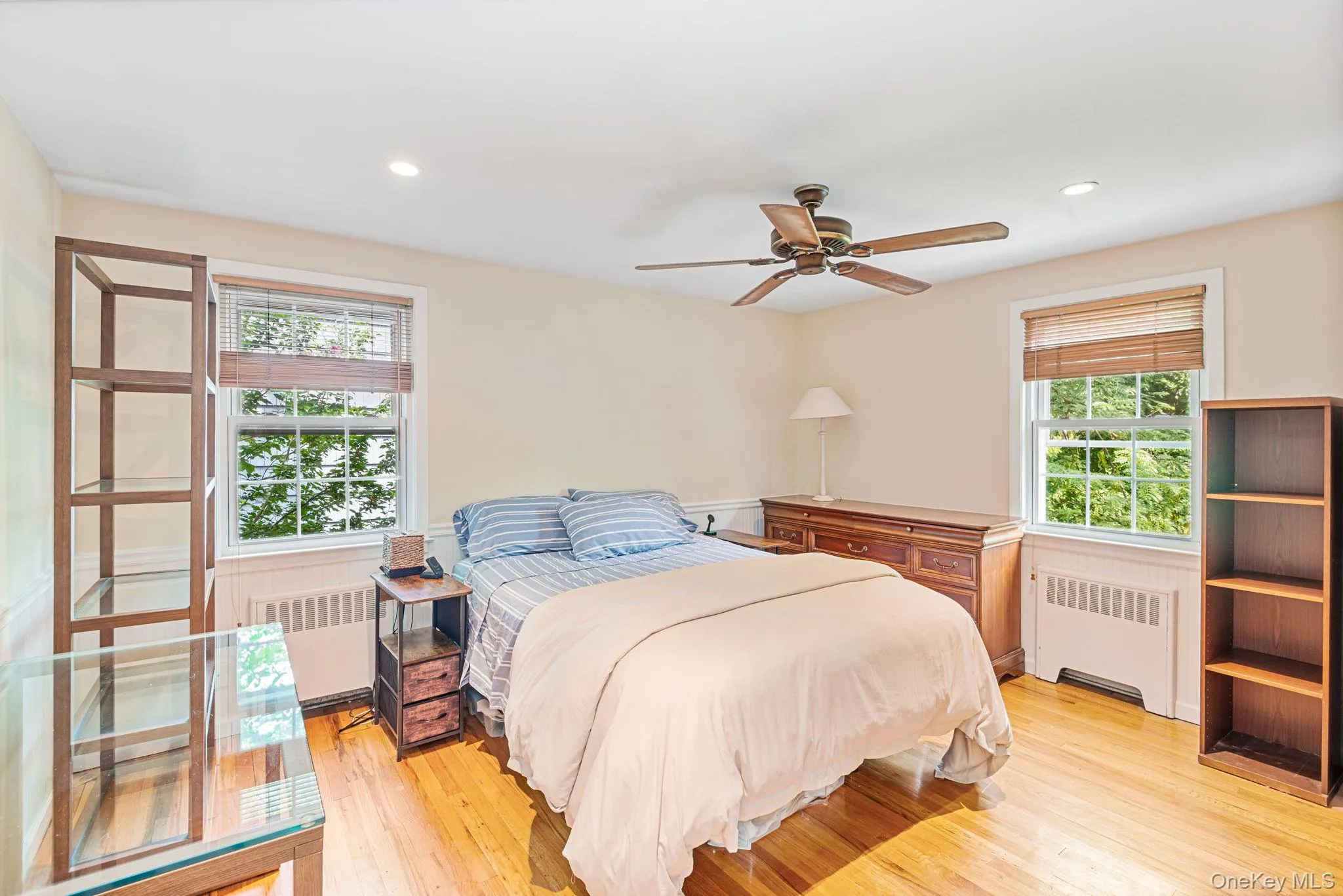 Bedroom with polished hardwood flooring, two windows with natural light, recessed lighting, and a ceiling fan Bedroom with polished hardwood flooring, two windows with natural light, recessed lighting, and a ceiling fan