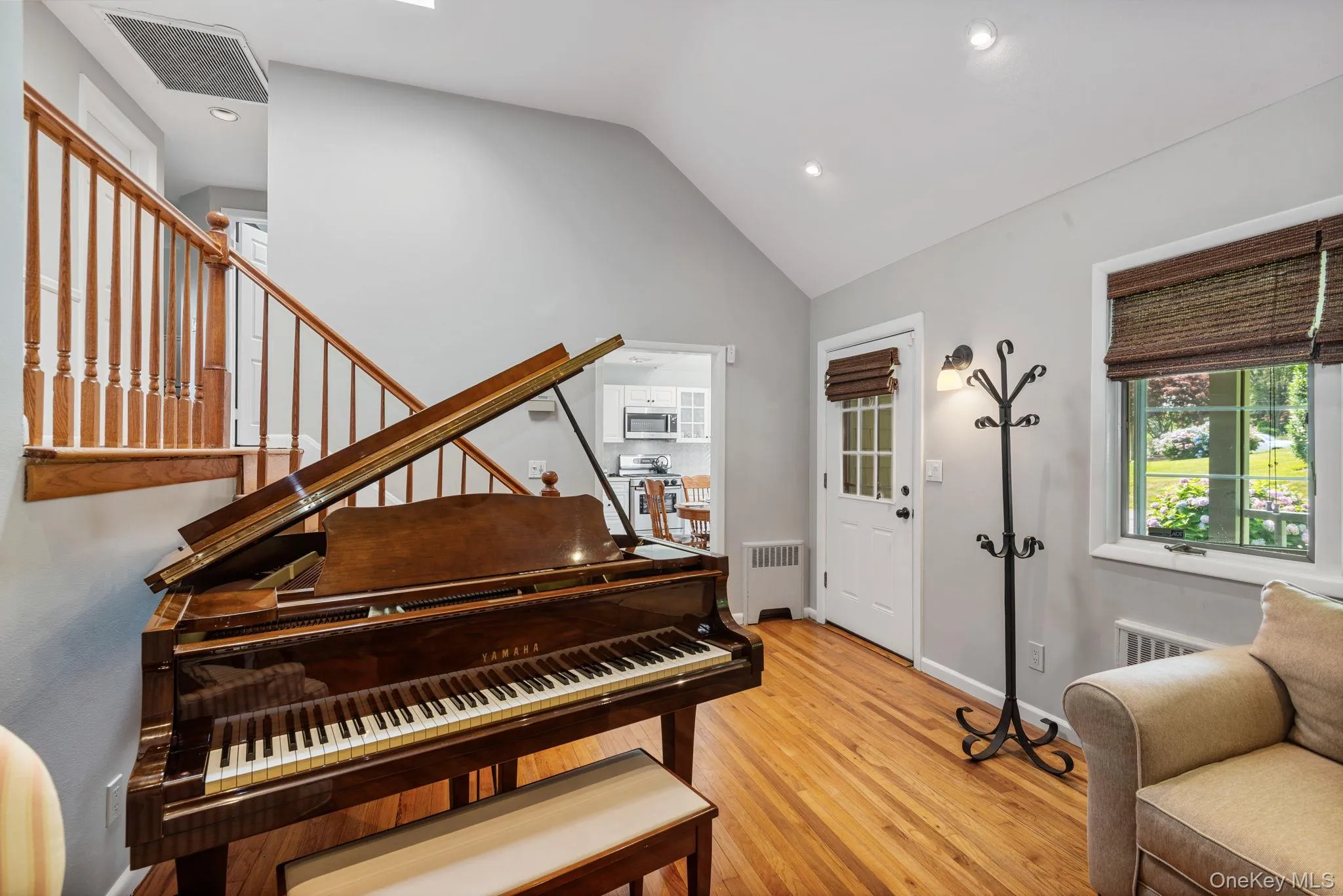 Front entrance into living space featuring hardwood flooring, vaulted ceiling with recessed lighting, and a staircase with a wooden banister Front entrance into living space featuring hardwood flooring, vaulted ceiling with recessed lighting, and a staircase with a wooden banister