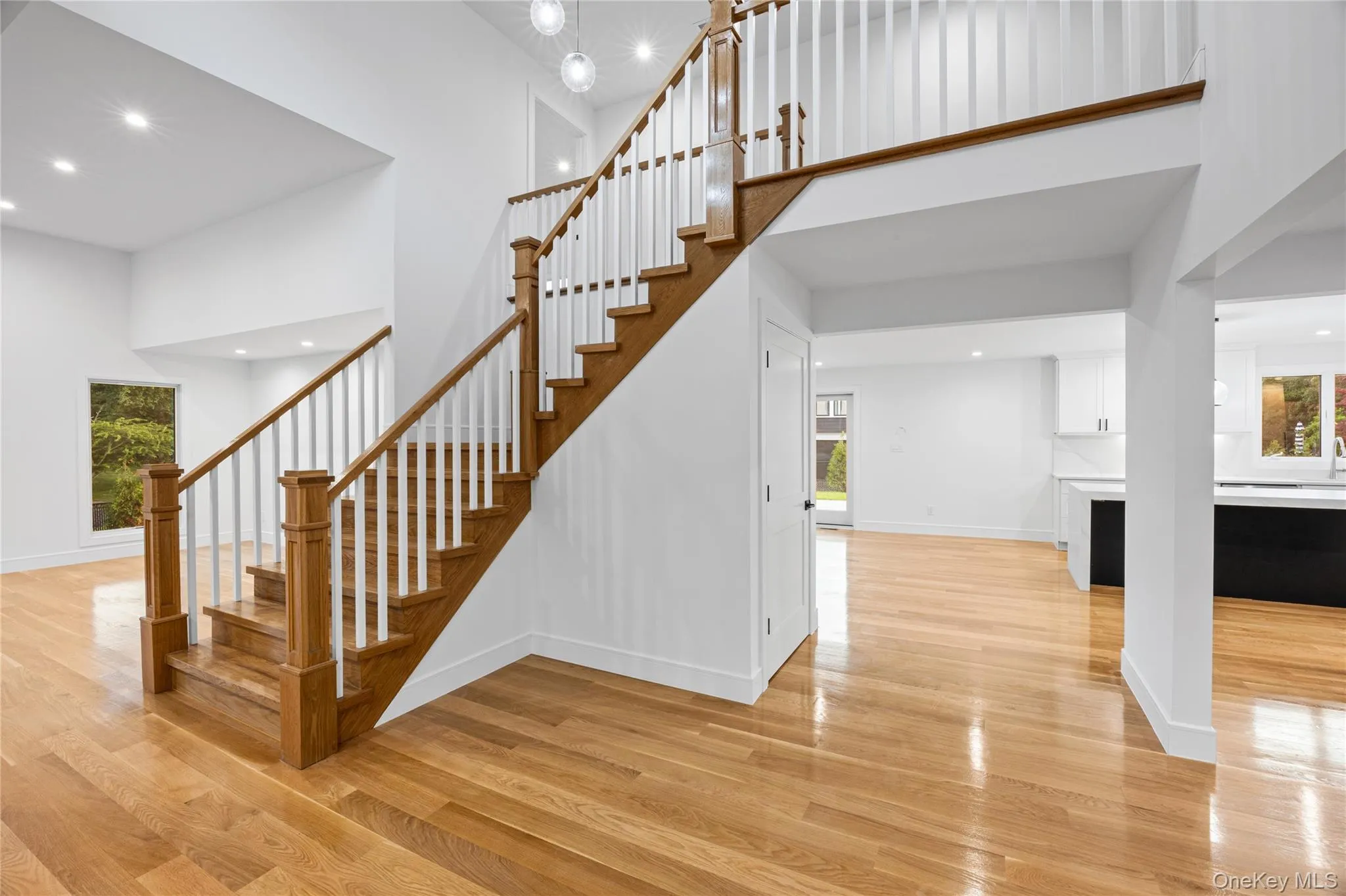 Two-story foyer featuring a hardwood staircase with white risers and spindles, high ceilings, recessed lighting, and polished wood-finish flooring Two-story foyer featuring a hardwood staircase with white risers and spindles, high ceilings, recessed lighting, and polished wood-finish flooring