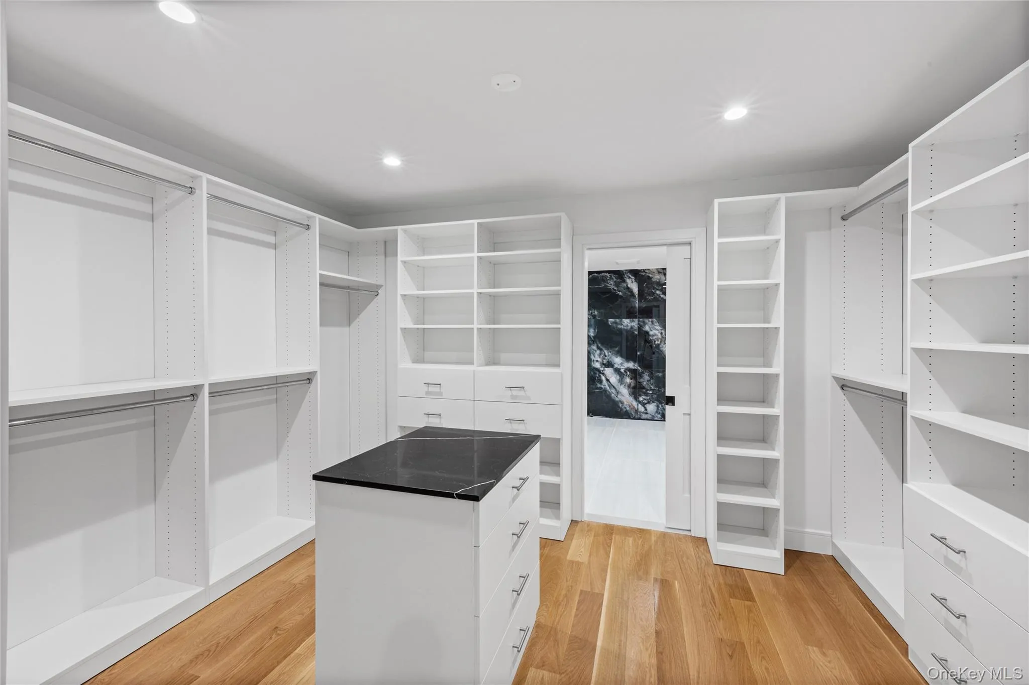 Spacious walk-in closet featuring extensive built-in shelving, multiple hanging rods, and an island with a dark stone countertop Spacious walk-in closet featuring extensive built-in shelving, multiple hanging rods, and an island with a dark stone countertop