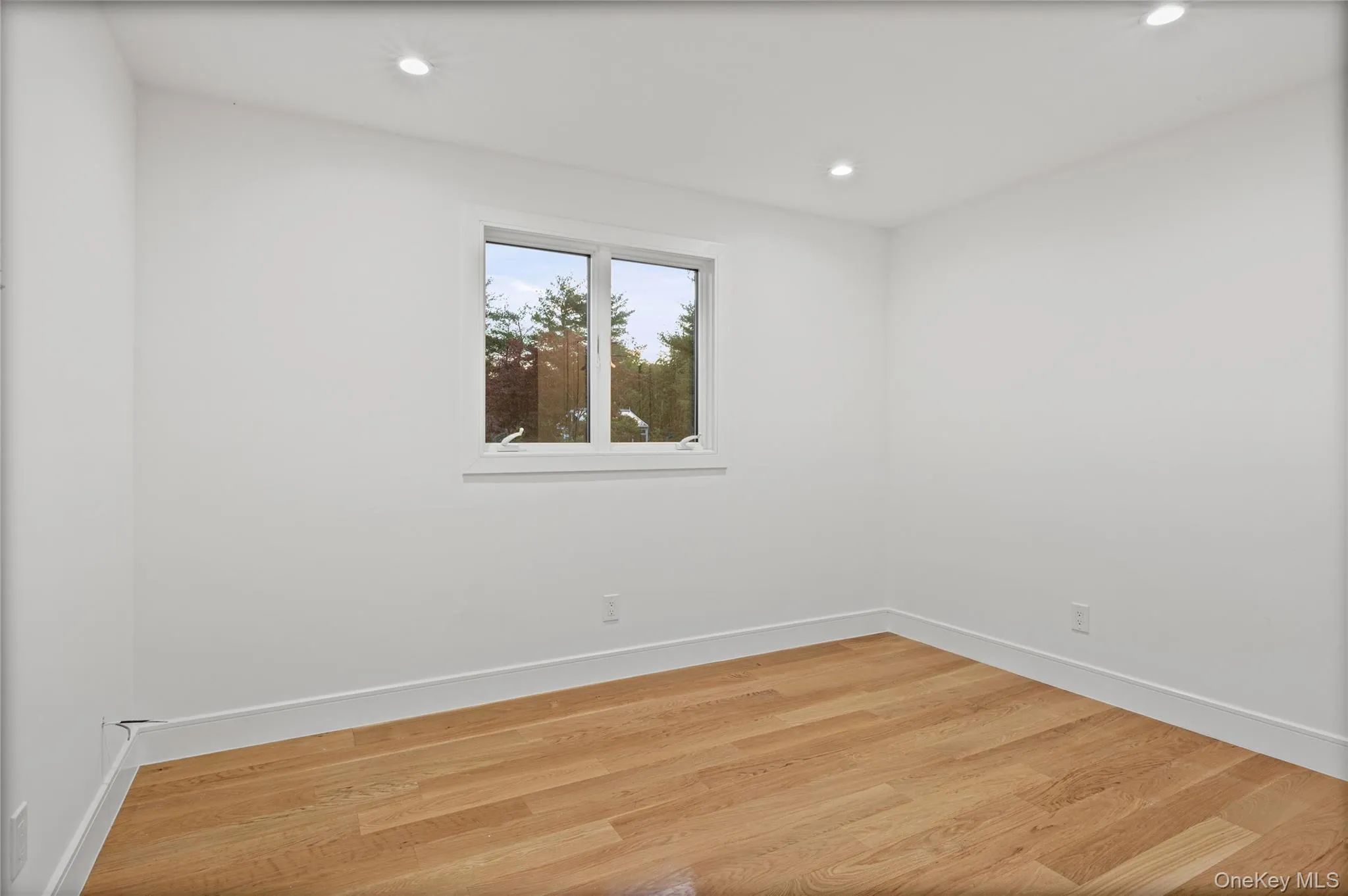 Room featuring a large window, light wood-finish flooring, white walls, white baseboards, and recessed lighting Room featuring a large window, light wood-finish flooring, white walls, white baseboards, and recessed lighting