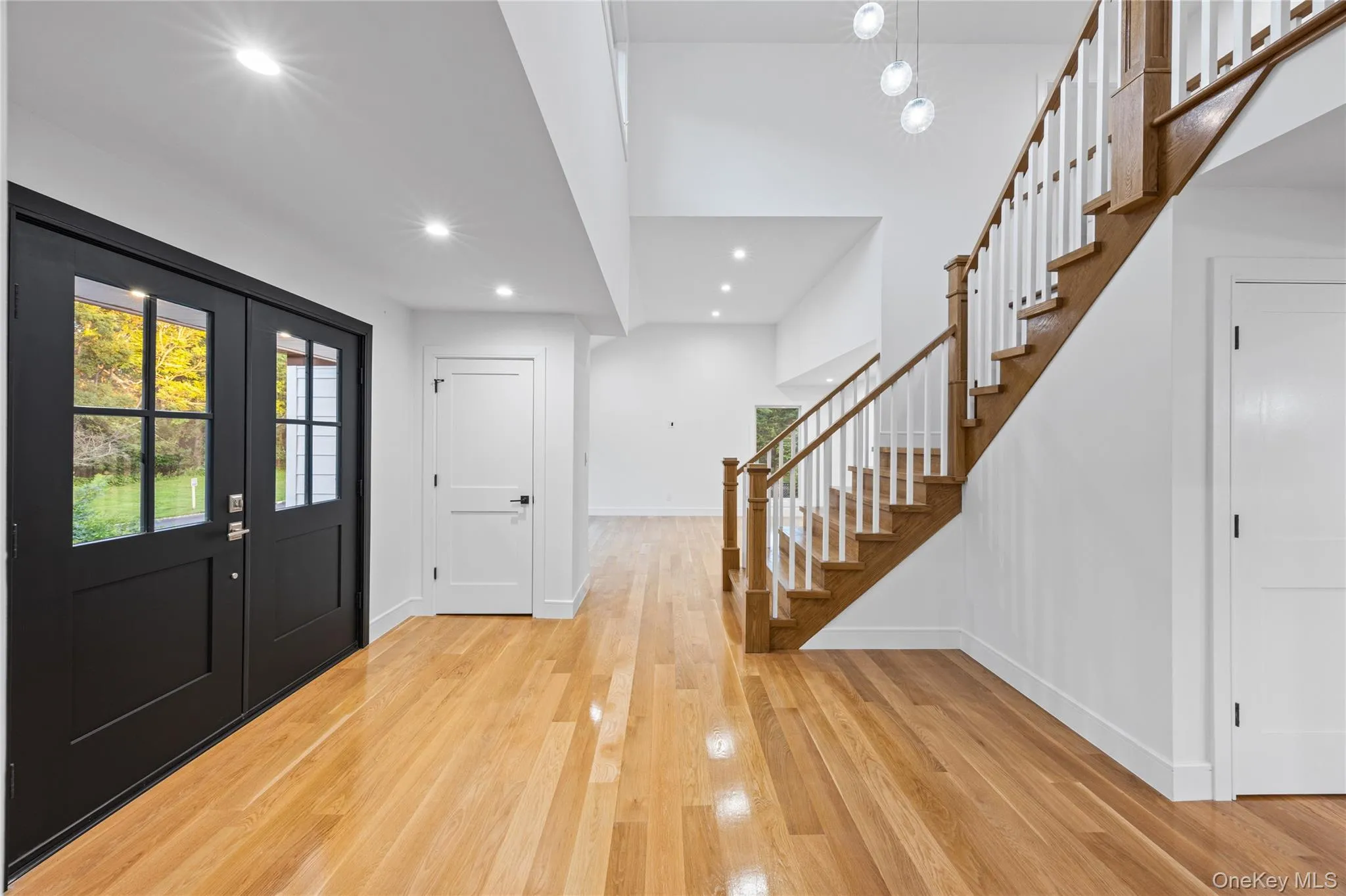 Entryway featuring wood-finish flooring, a grand staircase with wood and white balusters, recessed lighting, and a modern chandelier Entryway featuring wood-finish flooring, a grand staircase with wood and white balusters, recessed lighting, and a modern chandelier