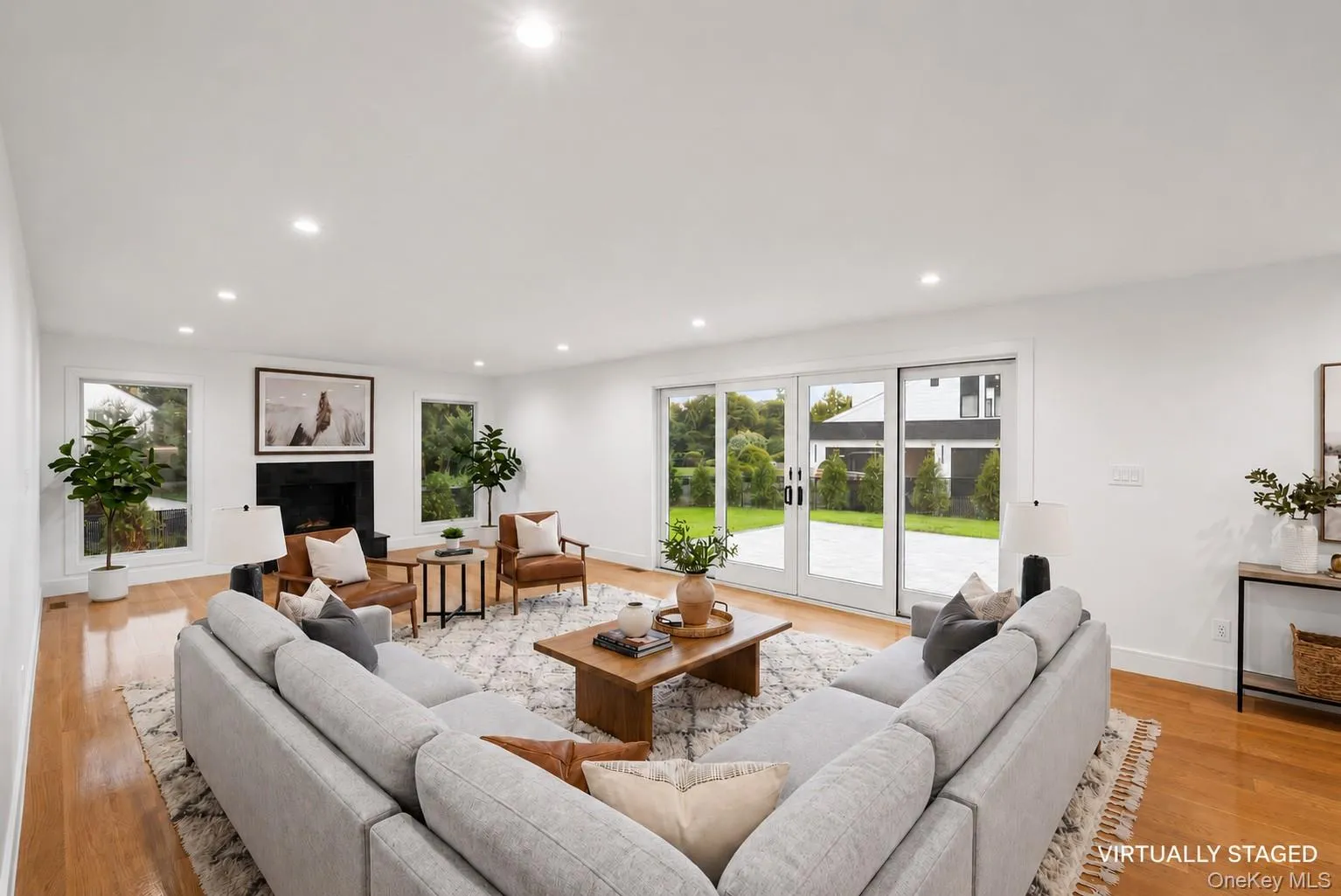Spacious living area featuring light wood-finish flooring, recessed lighting, and a prominent fireplace with a dark surround. Virtually Staged. Spacious living area featuring light wood-finish flooring, recessed lighting, and a prominent fireplace with a dark surround. Virtually Staged.