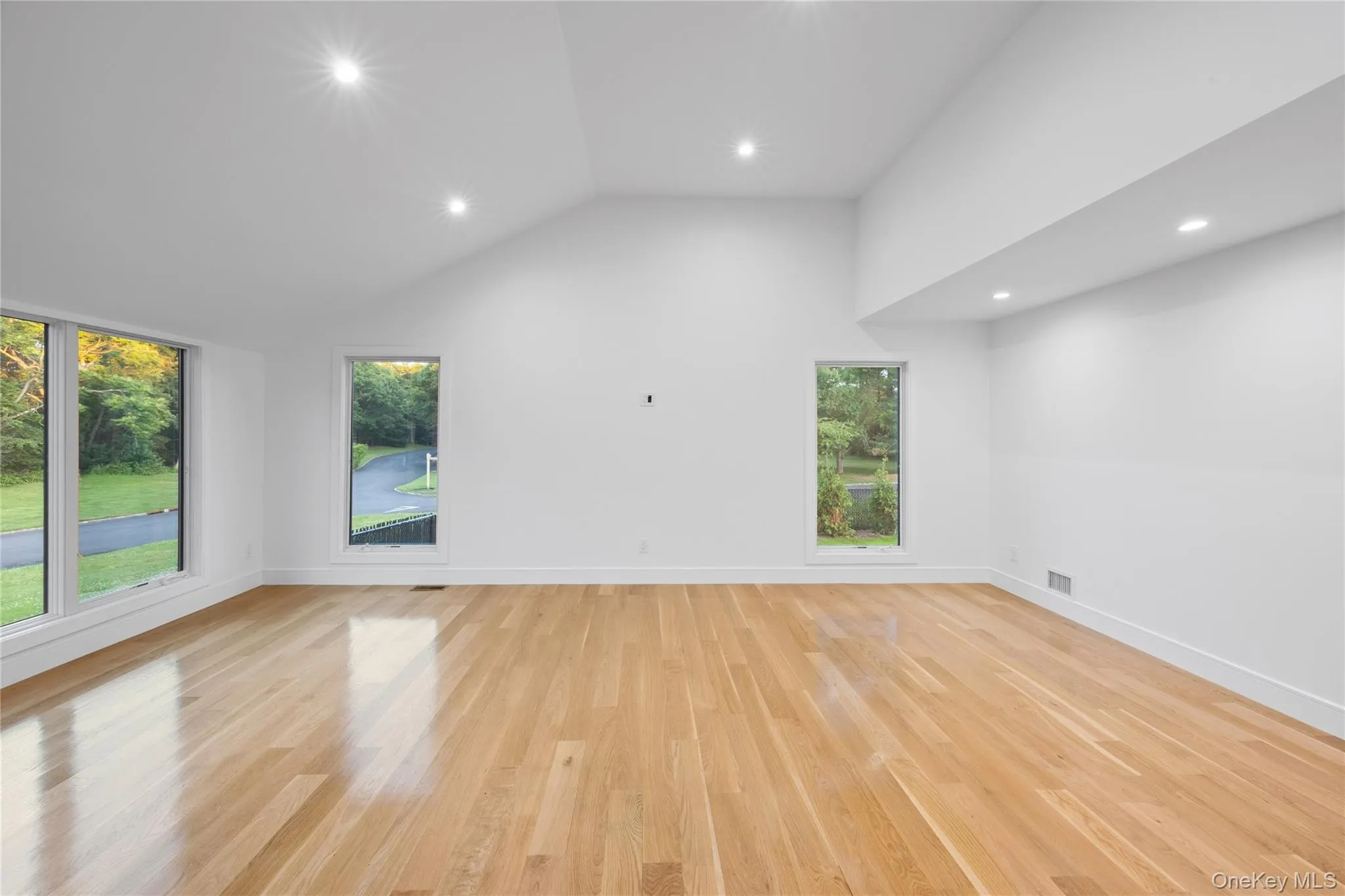 Spacious living area featuring a vaulted ceiling, recessed lighting, expansive windows, light wood-finish flooring. Spacious living area featuring a vaulted ceiling, recessed lighting, expansive windows, light wood-finish flooring.