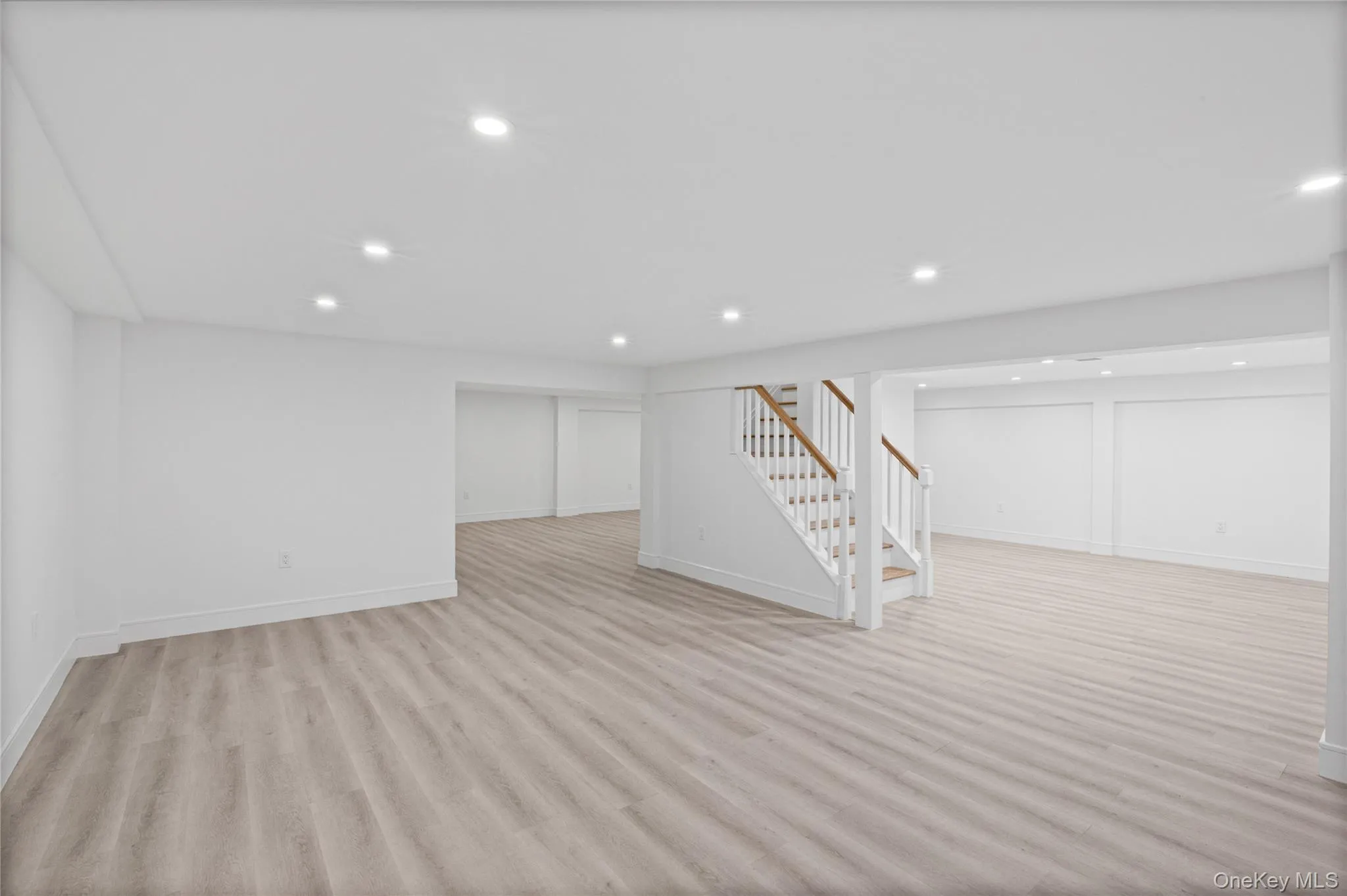 Spacious lower level featuring light wood-finish flooring, recessed lighting, and a white baluster staircase with wood handrails Spacious lower level featuring light wood-finish flooring, recessed lighting, and a white baluster staircase with wood handrails