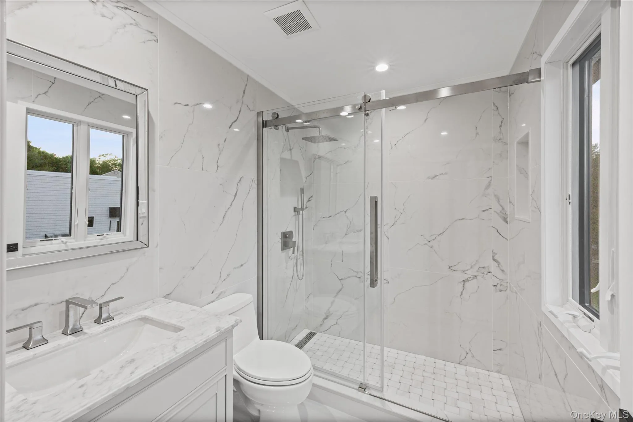 En-Suite bathroom featuring a walk-in shower with glass enclosure, white marble-look tile, recessed lighting, a window, and a vanity with a rectangular sink En-Suite bathroom featuring a walk-in shower with glass enclosure, white marble-look tile, recessed lighting, a window, and a vanity with a rectangular sink