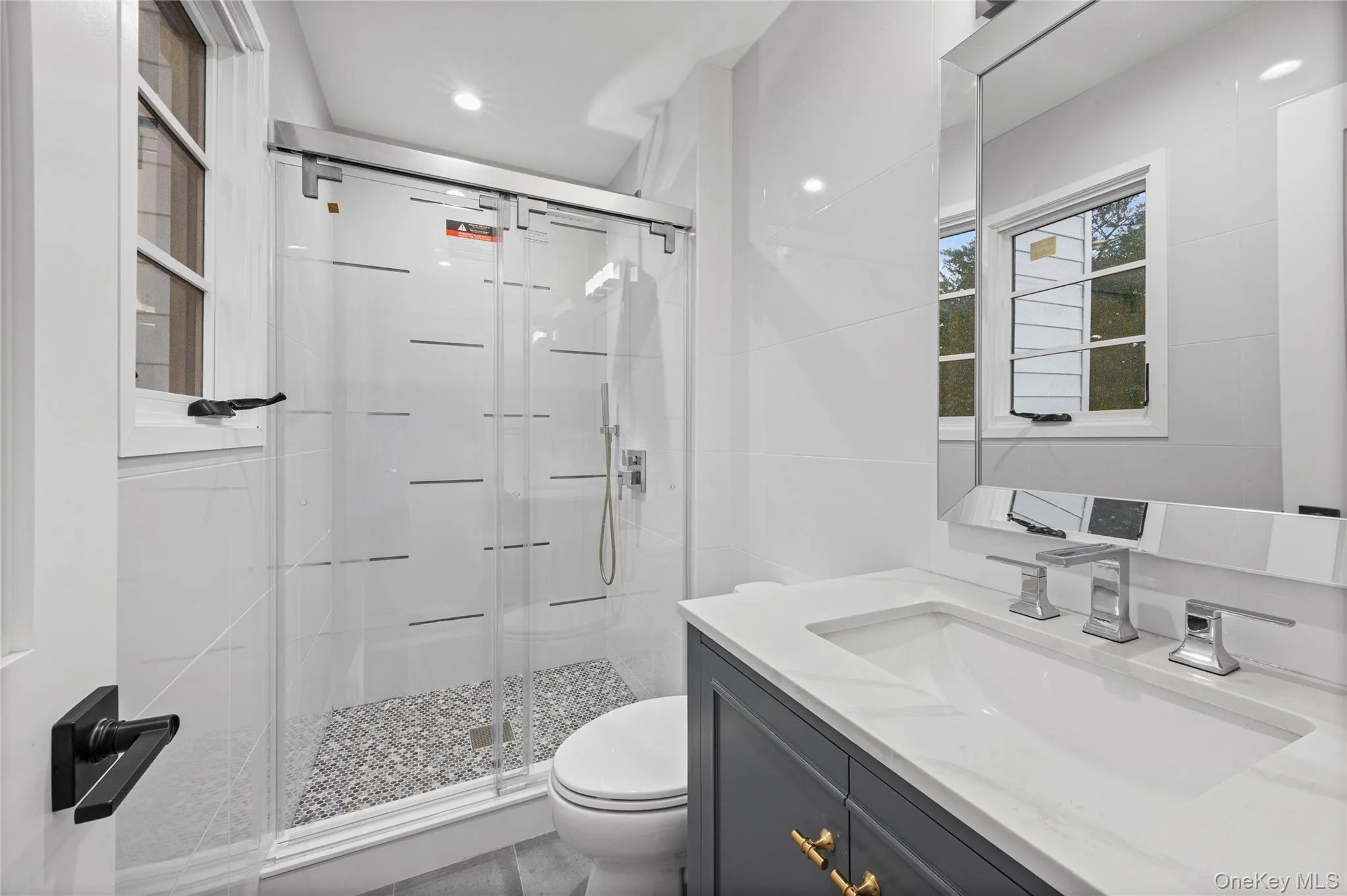 Contemporary bathroom featuring a dark grey vanity with gold-tone hardware, a white countertop with an integrated sink, and a chrome faucet. Located on ground floor next to mud room and ground floor bedroom. Contemporary bathroom featuring a dark grey vanity with gold-tone hardware, a white countertop with an integrated sink, and a chrome faucet. Located on ground floor next to mud room and ground floor bedroom.
