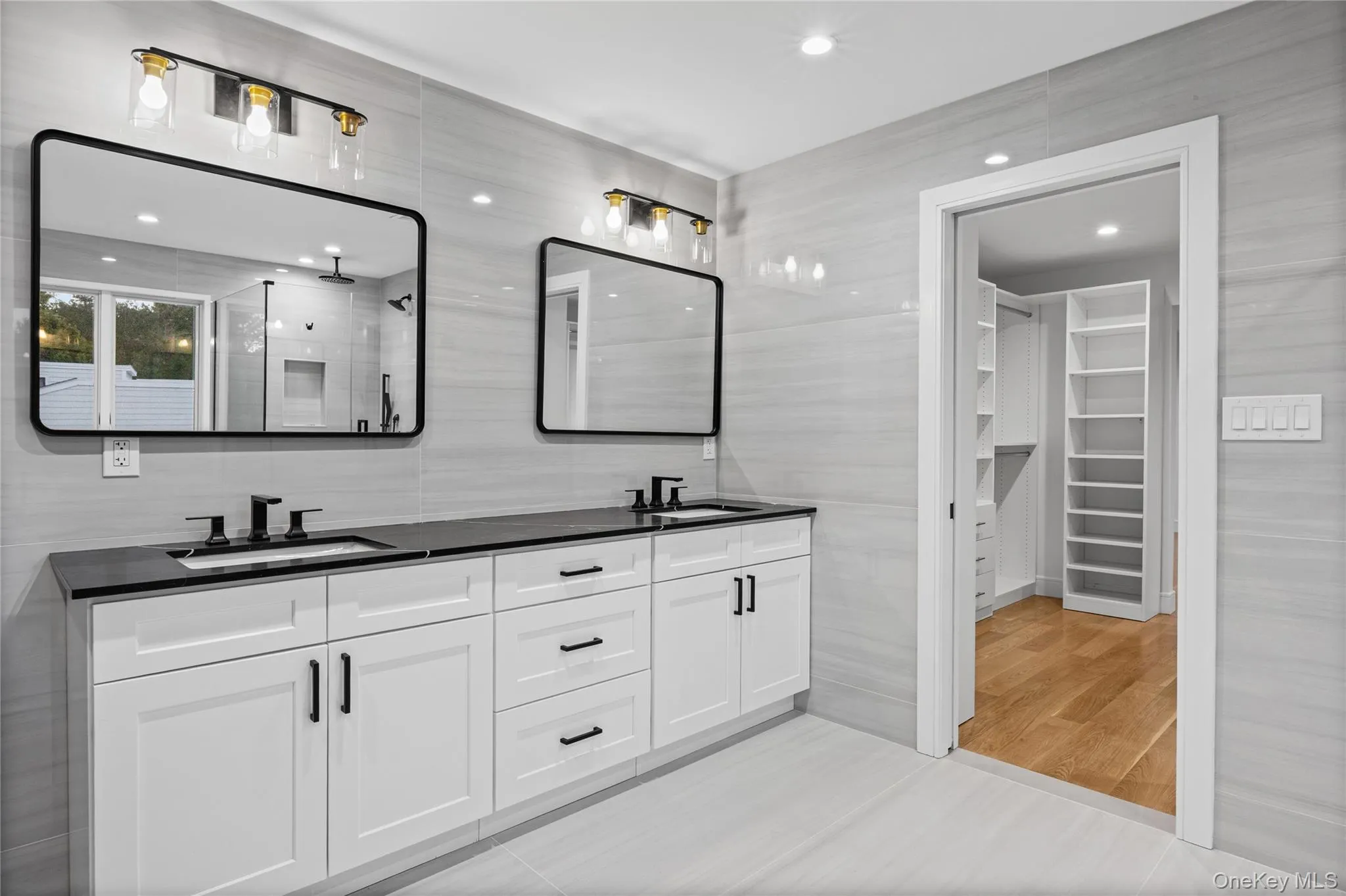Contemporary bathroom featuring a dual vanity with white shaker-style cabinetry, black countertops, and matte black fixtures Contemporary bathroom featuring a dual vanity with white shaker-style cabinetry, black countertops, and matte black fixtures